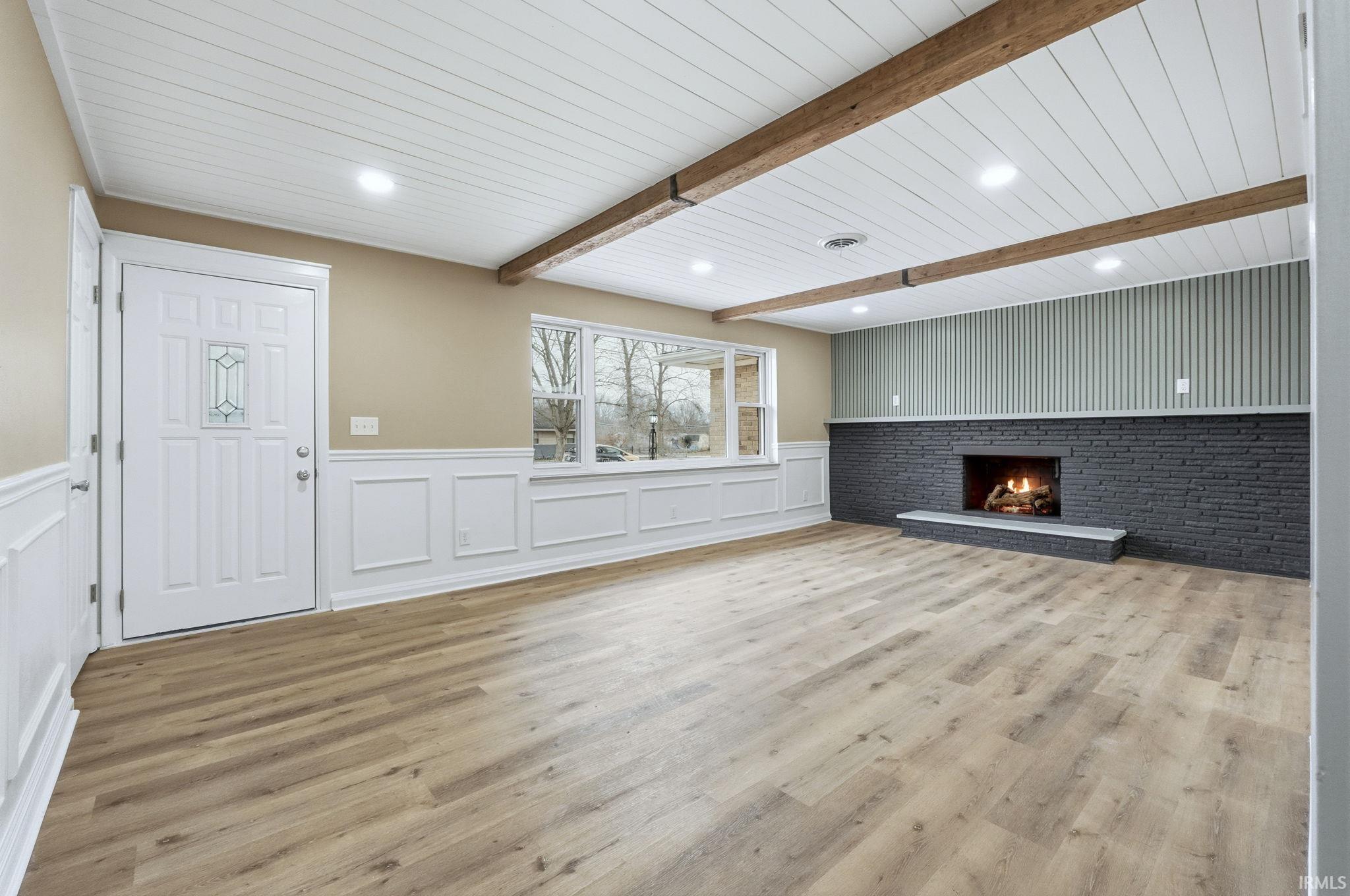 Unfurnished living room featuring wainscoting, light wood-style floors, a brick fireplace, a decorative wall, and recessed lighting