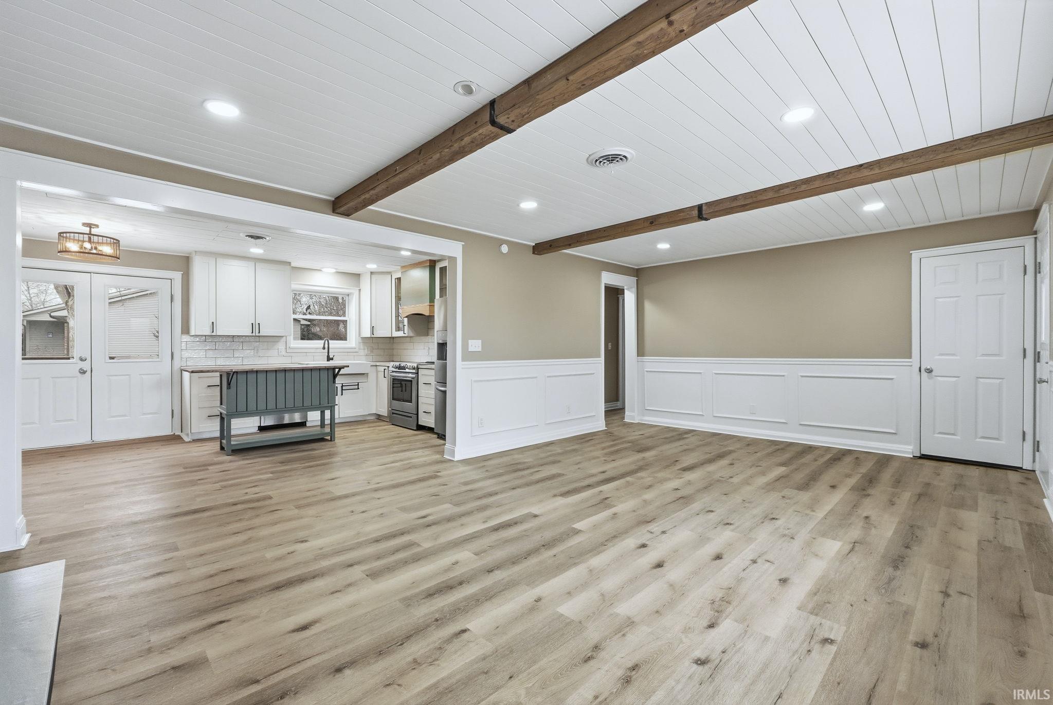 Unfurnished living room with a decorative wall, a wainscoted wall, light wood-type flooring, beam ceiling, and recessed lighting