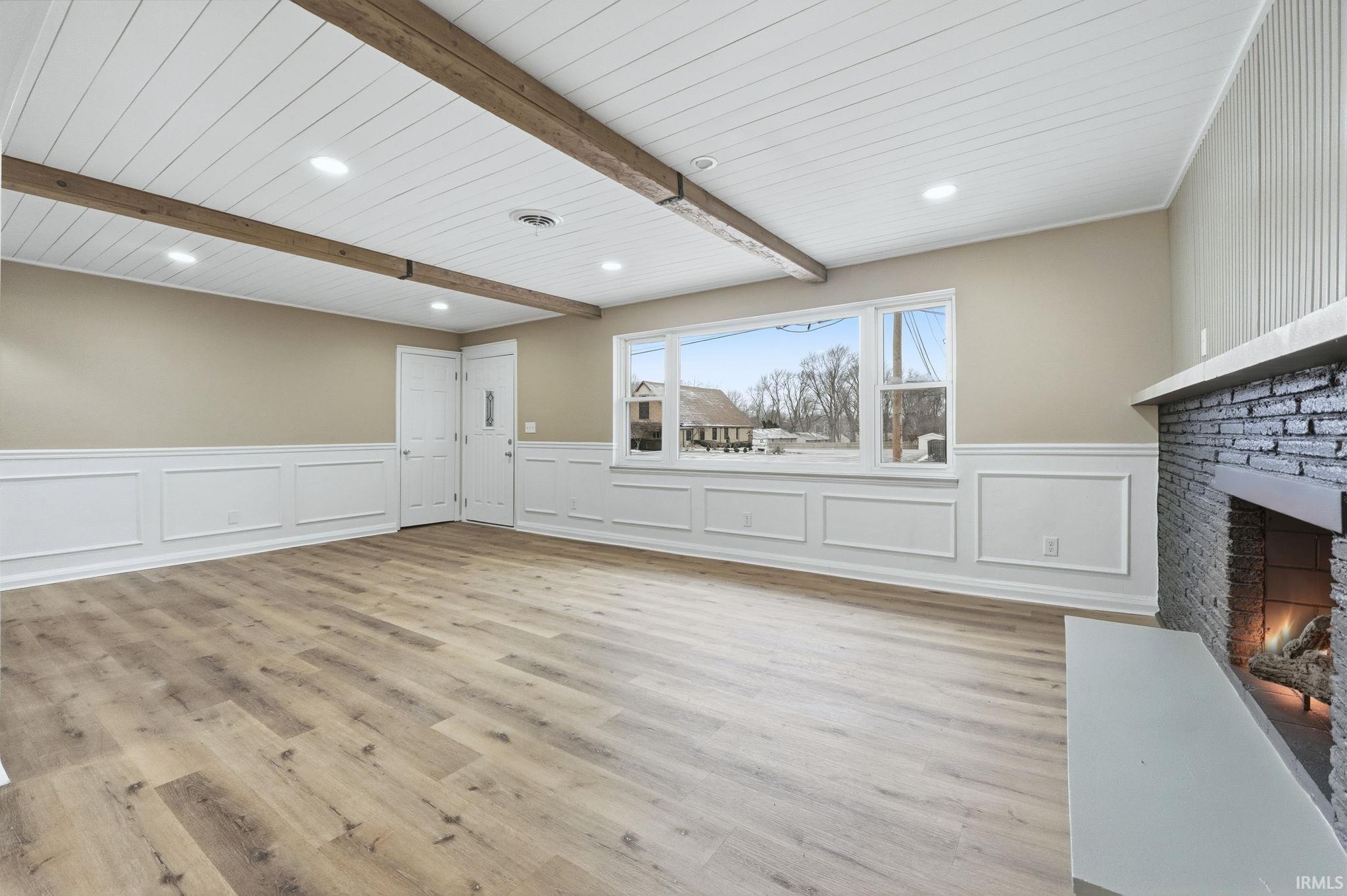 Unfurnished living room with a fireplace, light wood-style floors, wainscoting, a decorative wall, and recessed lighting