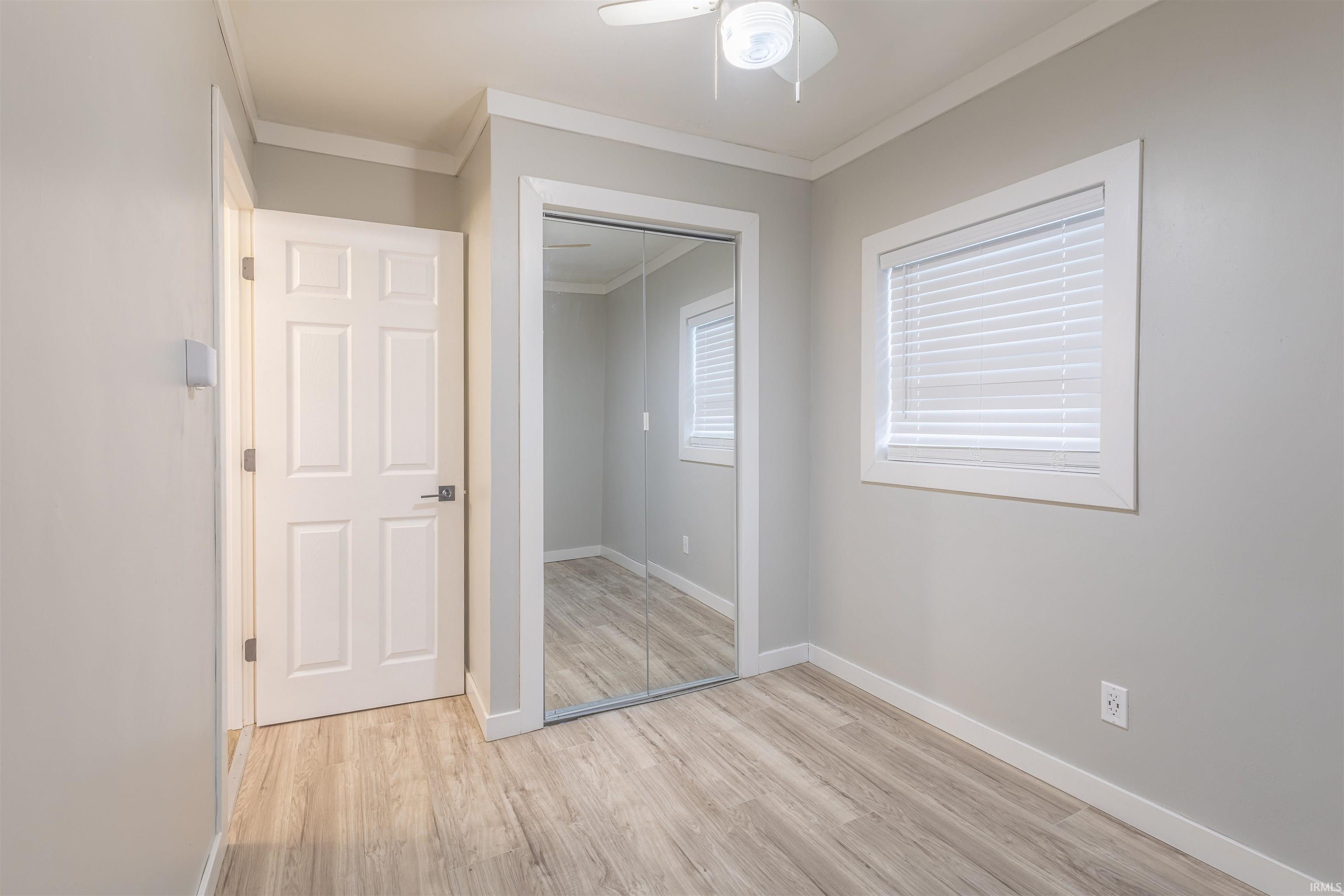 Unfurnished bedroom with crown molding, light wood finished floors, a closet, and ceiling fan