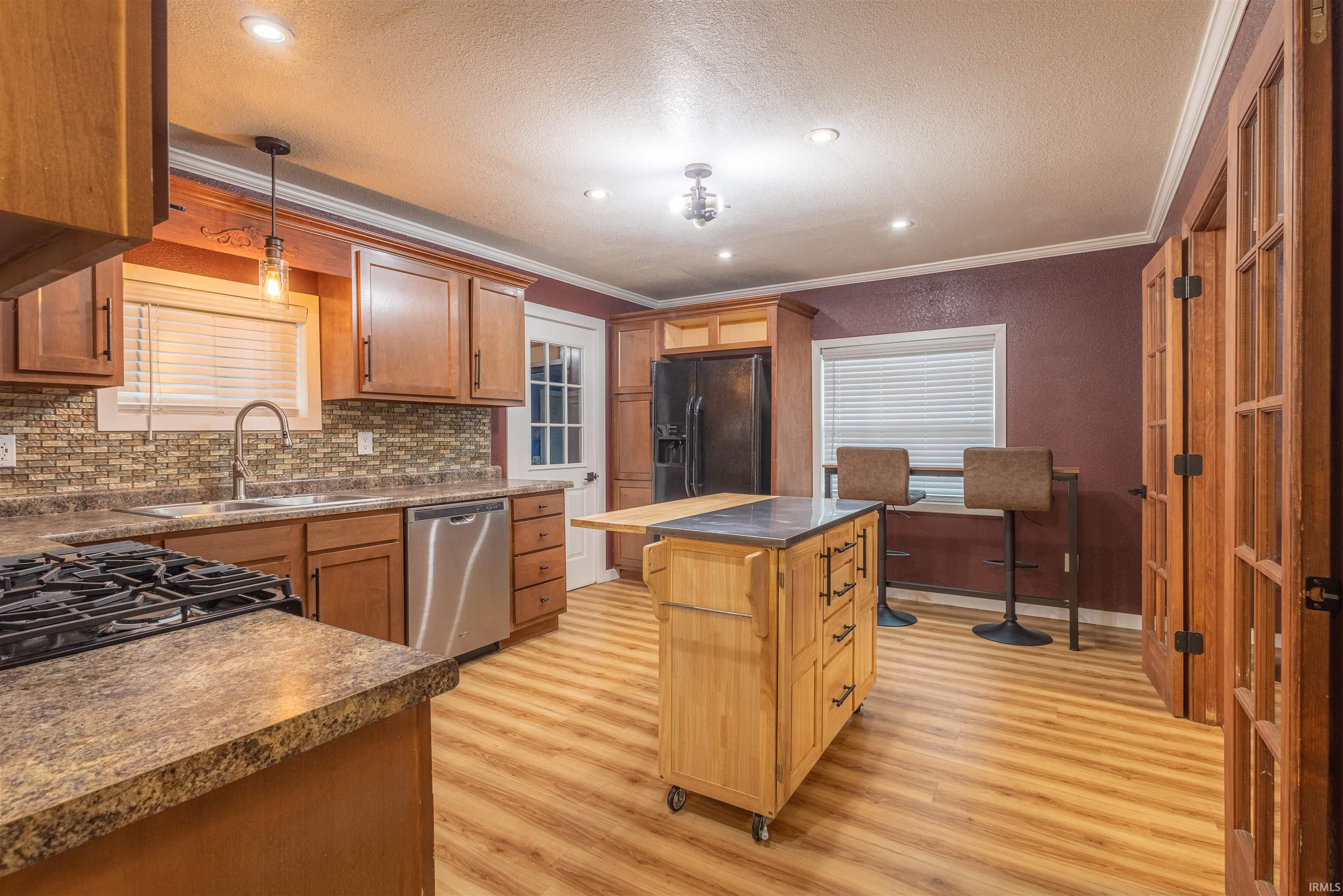 Kitchen featuring black fridge, hanging light fixtures, light wood finished floors, ornamental molding, and stainless steel dishwasher