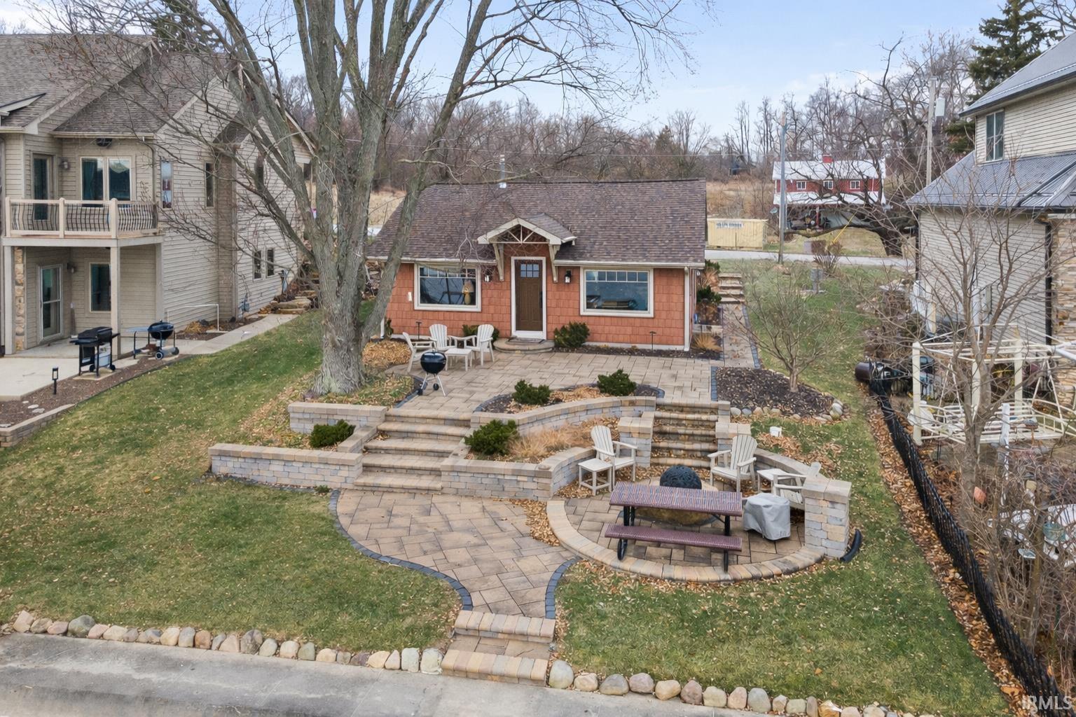 View of front of property featuring a patio, a front yard, roof with shingles, and a fire pit