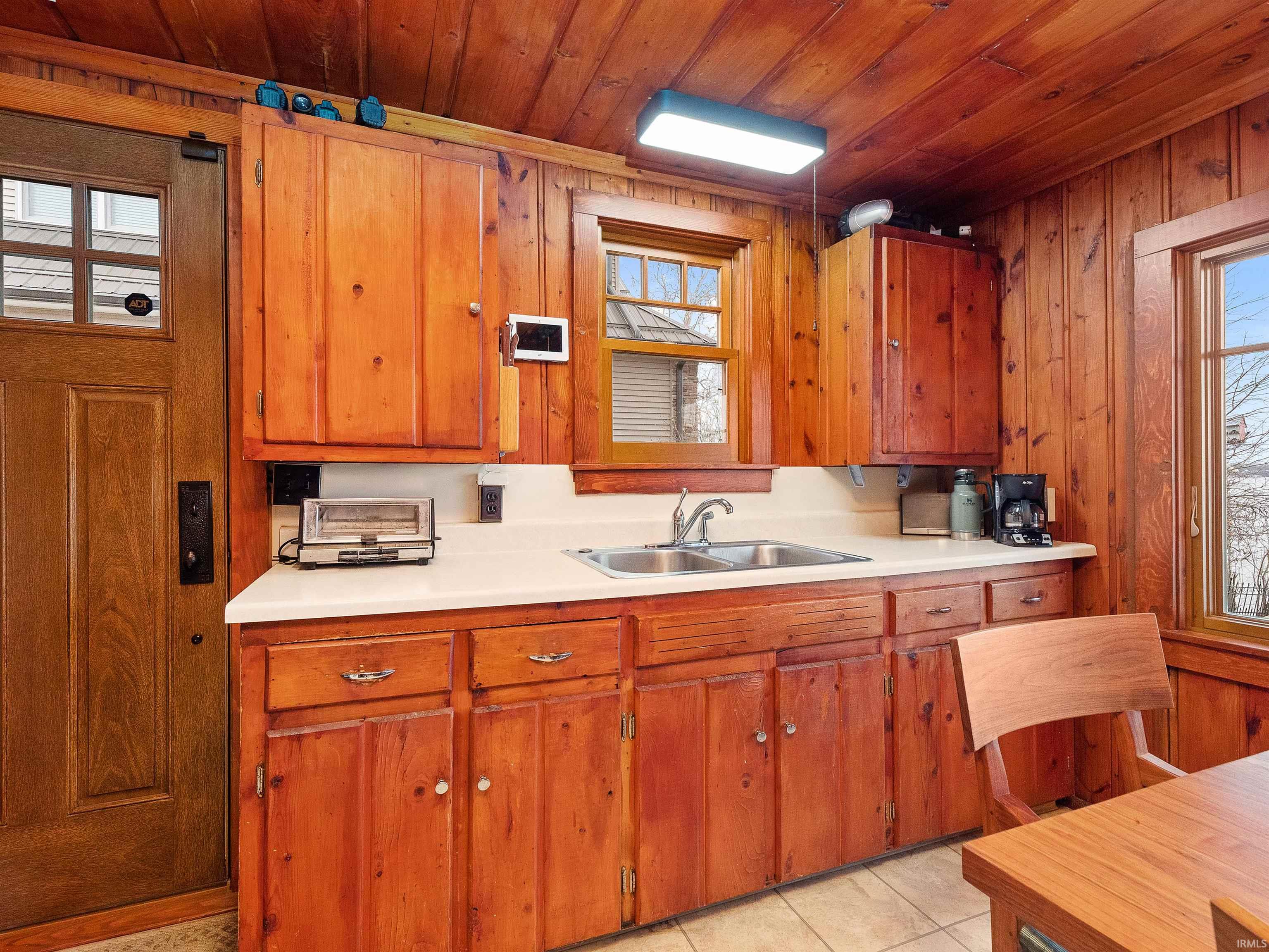 Kitchen with light countertops, wood ceiling, brown cabinetry, light tile patterned flooring, and wood walls