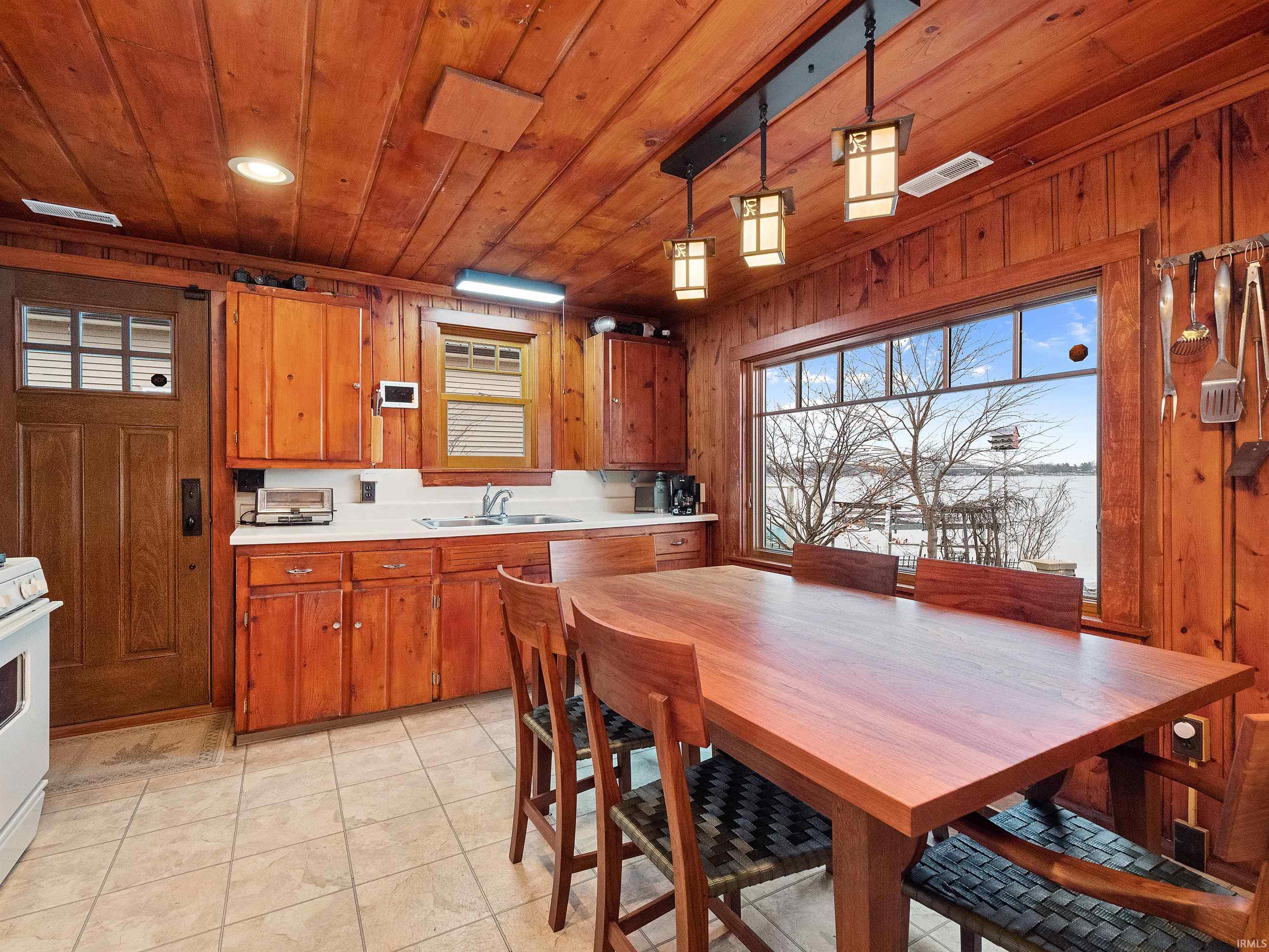 Kitchen featuring light countertops, pendant lighting, plenty of natural light, brown cabinets, and wooden ceiling