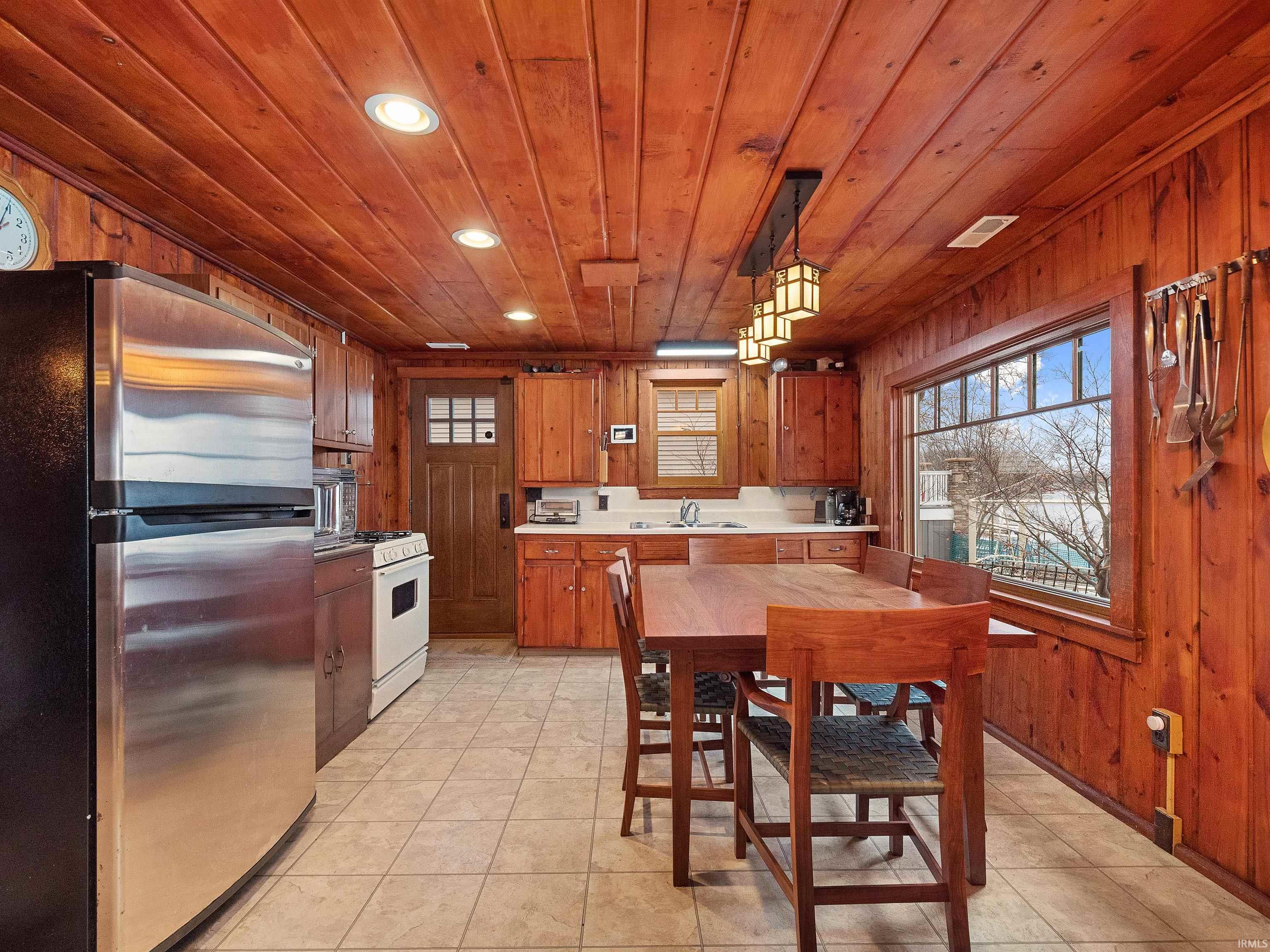 Kitchen featuring freestanding refrigerator, wooden walls, hanging light fixtures, light countertops, and wooden ceiling