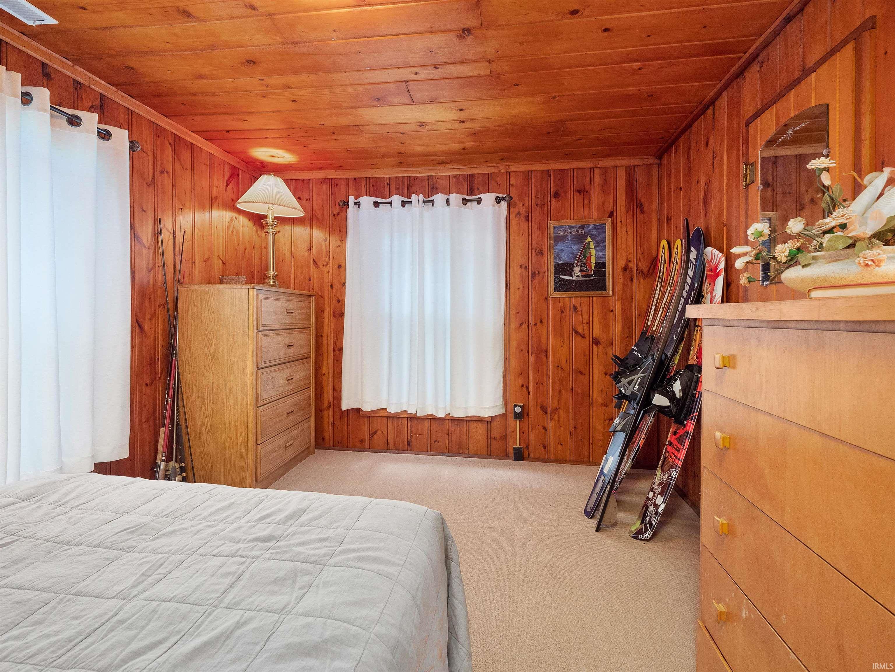 Bedroom featuring wood ceiling, light carpet, and wooden walls