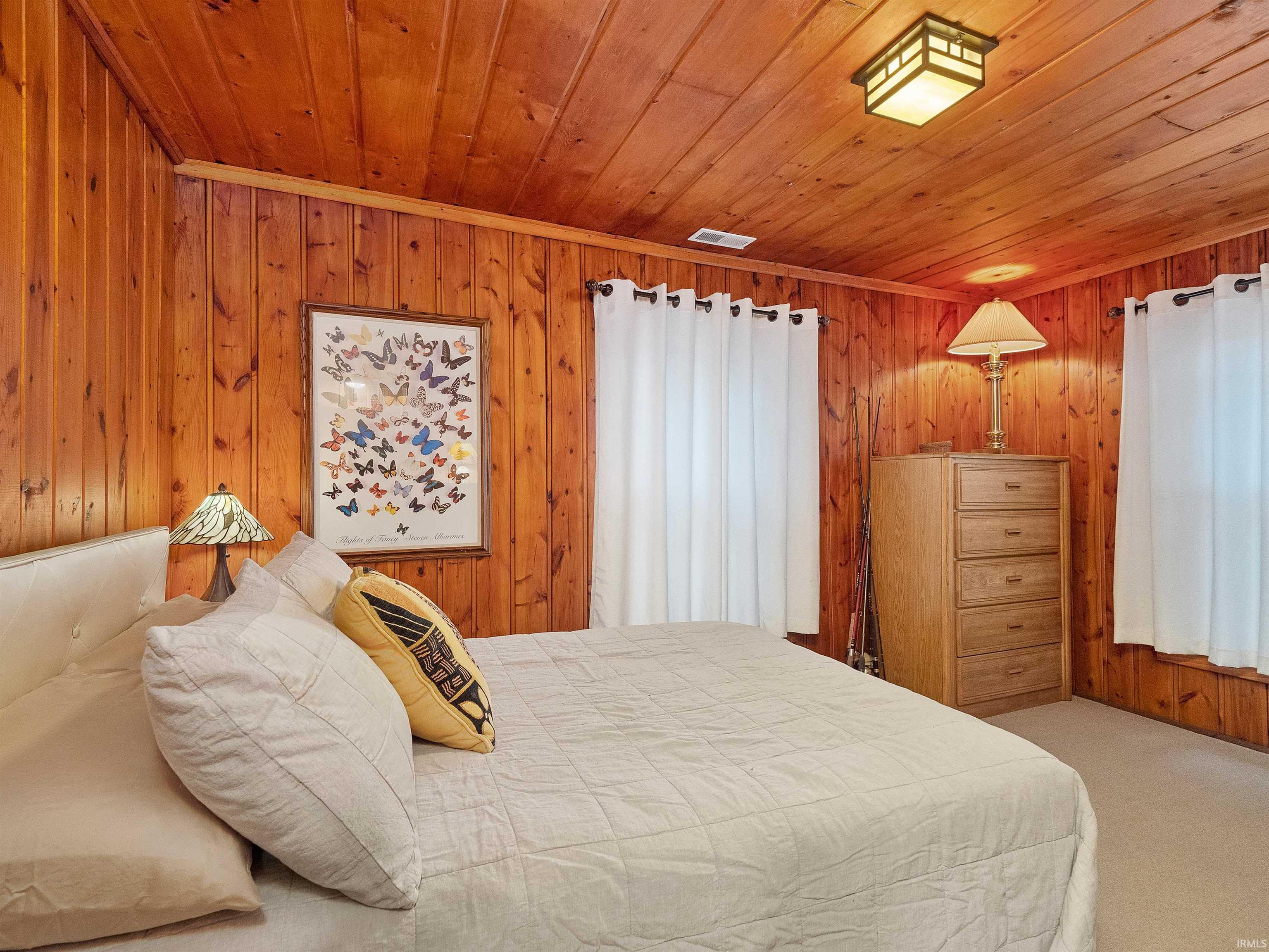 Carpeted bedroom featuring wood walls and wooden ceiling