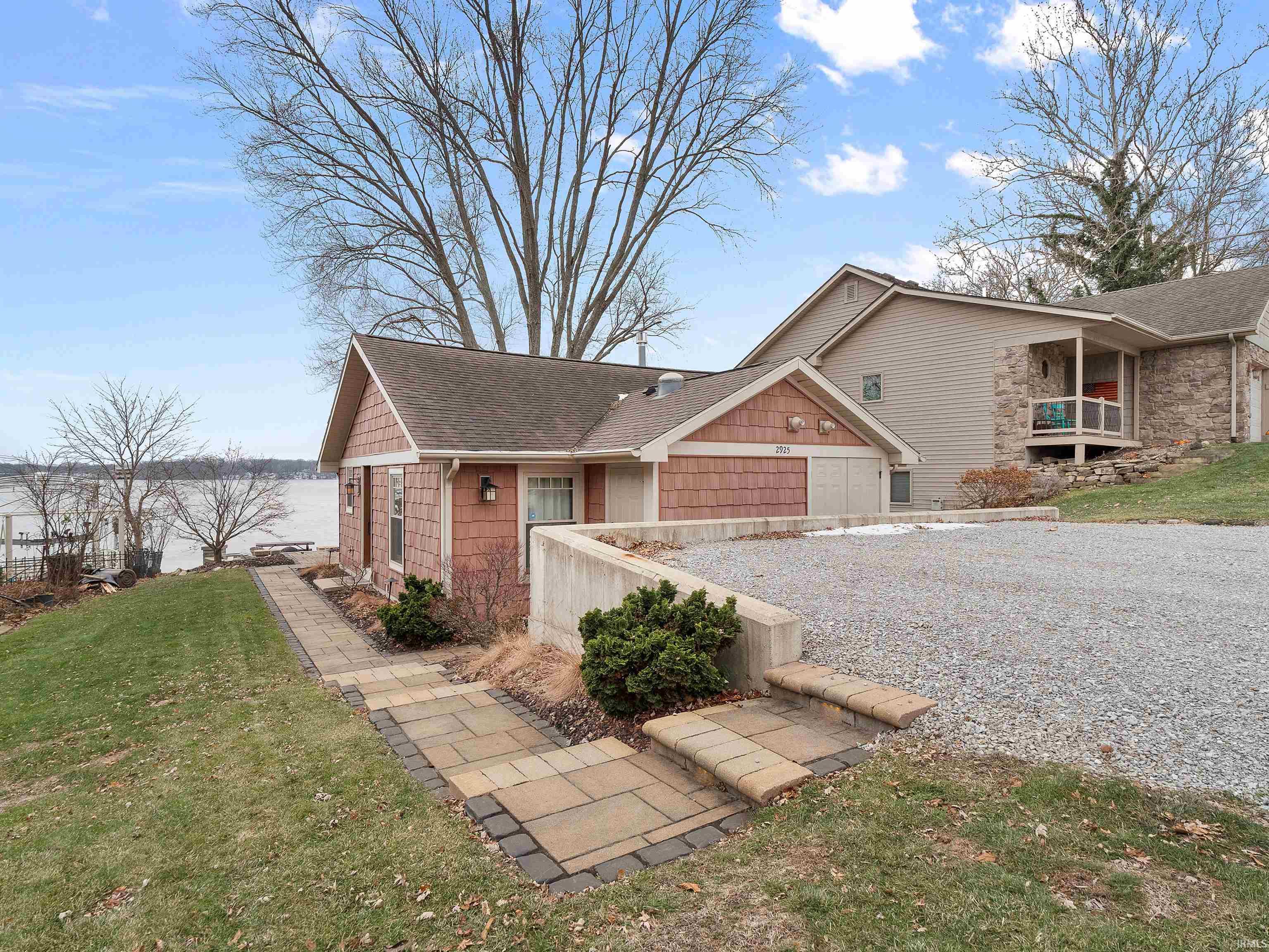 View of front of home with a shingled roof, a front yard, and gravel driveway