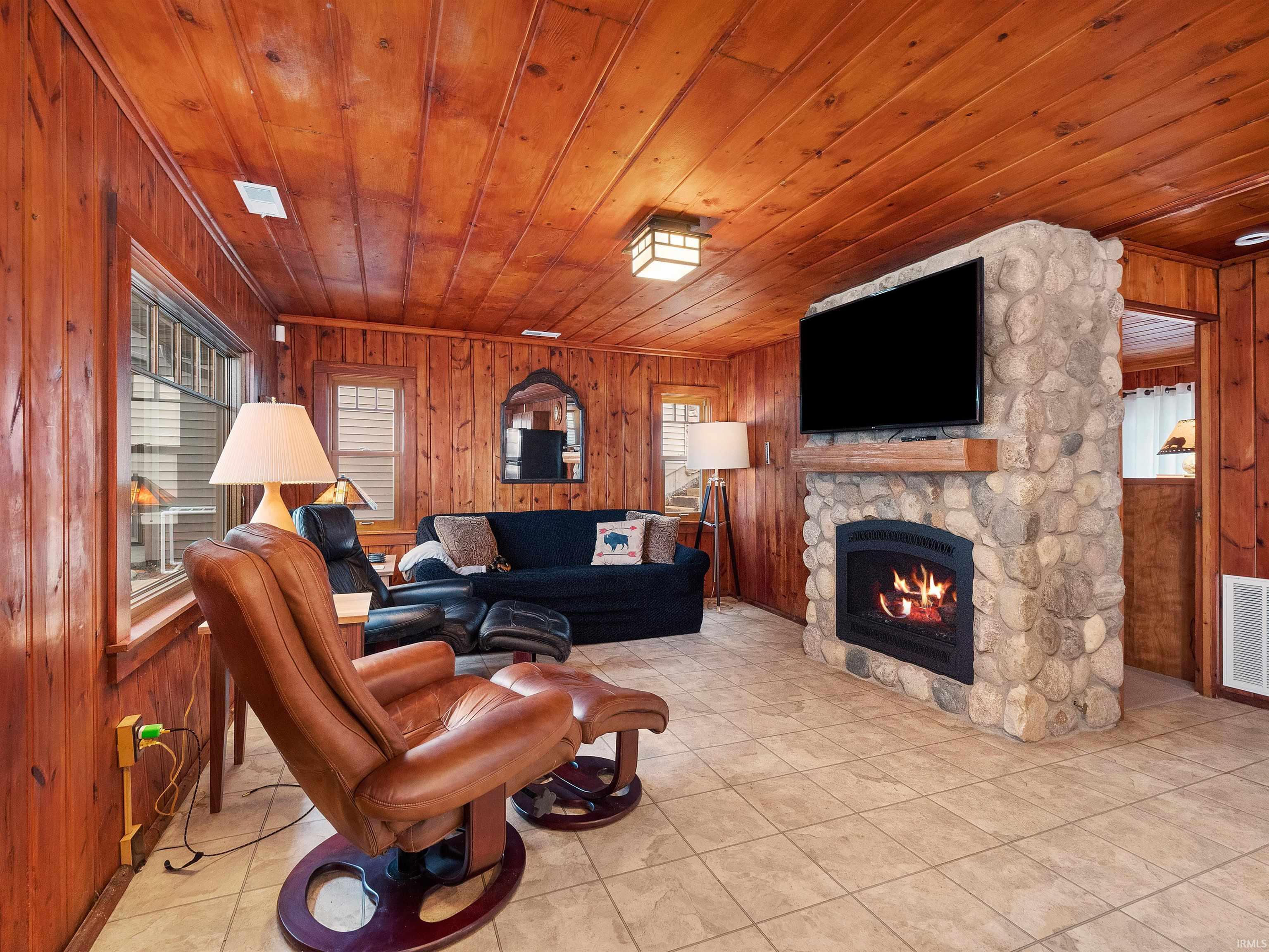 Tiled living area with a fireplace, wooden ceiling, and wooden walls