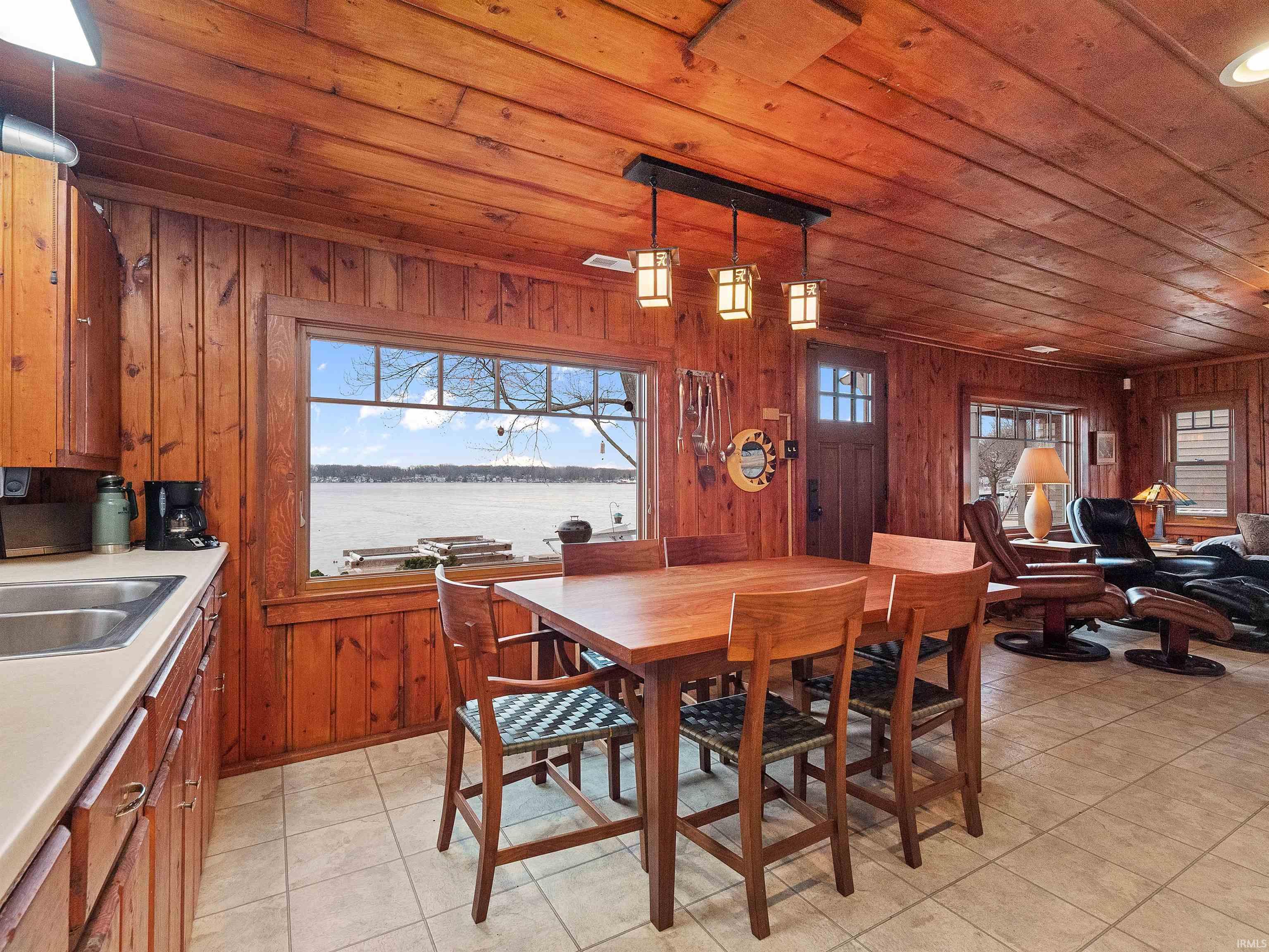 Dining room with a water view, wooden ceiling, light tile patterned floors, and wooden walls