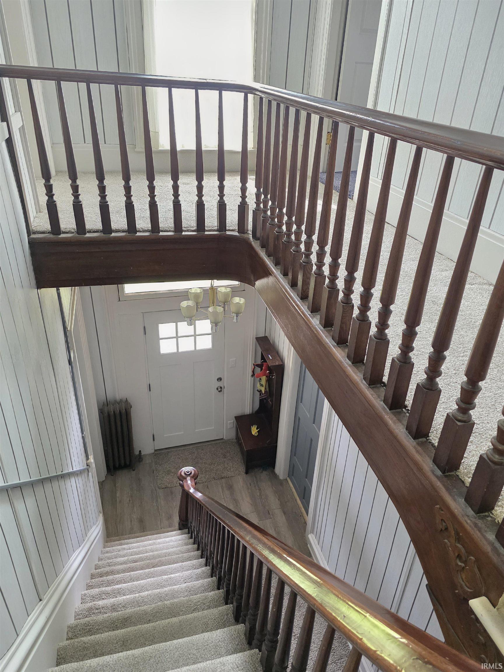 Multi-level interior featuring a carpeted staircase with a wood-finish handrail and balusters, leading to a landing with light wood-finish flooring