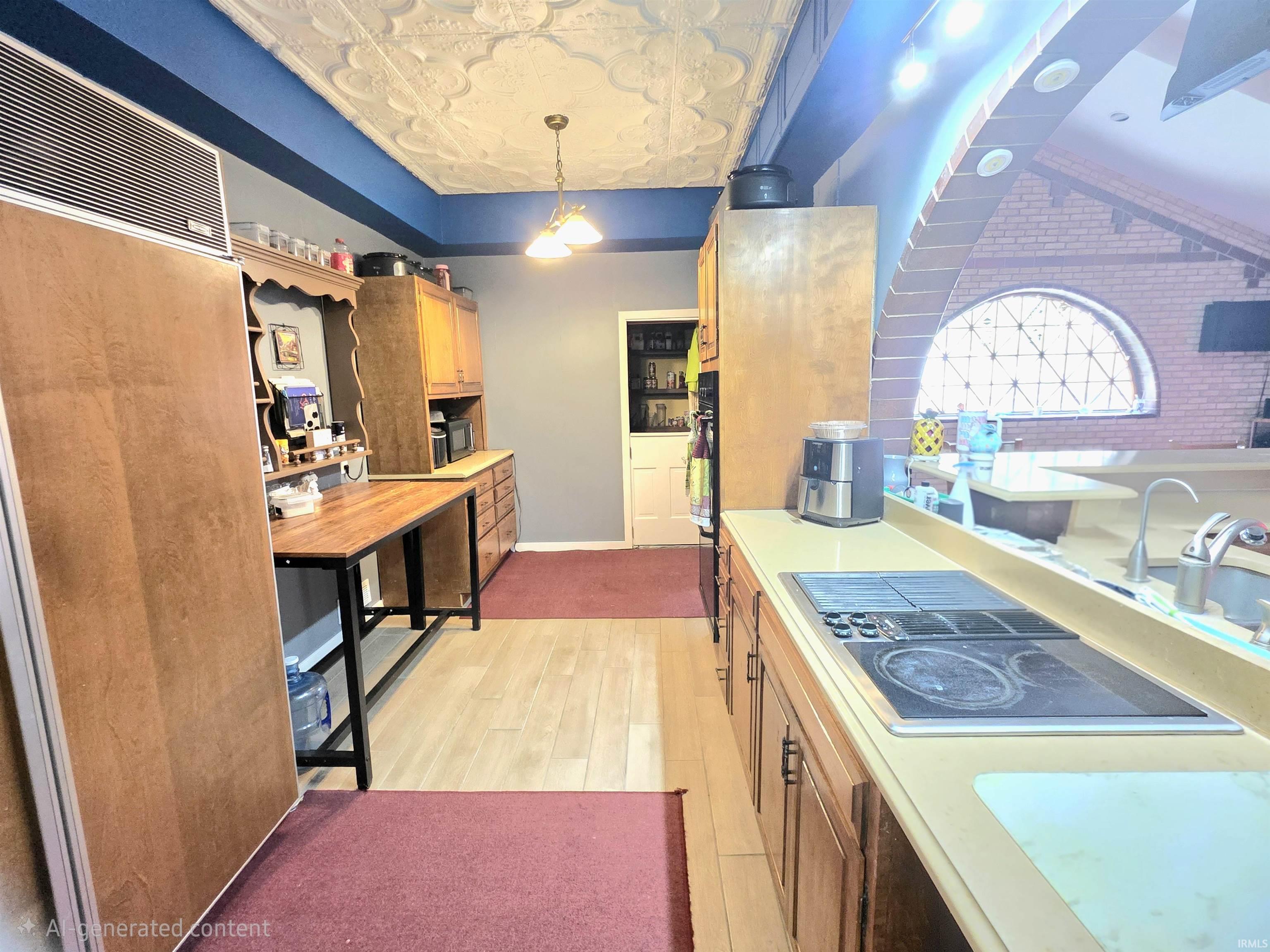 Galley kitchen featuring a pressed tin ceiling, wood-finish flooring, built-in cooktop, and an arched brick wall with an ornate window