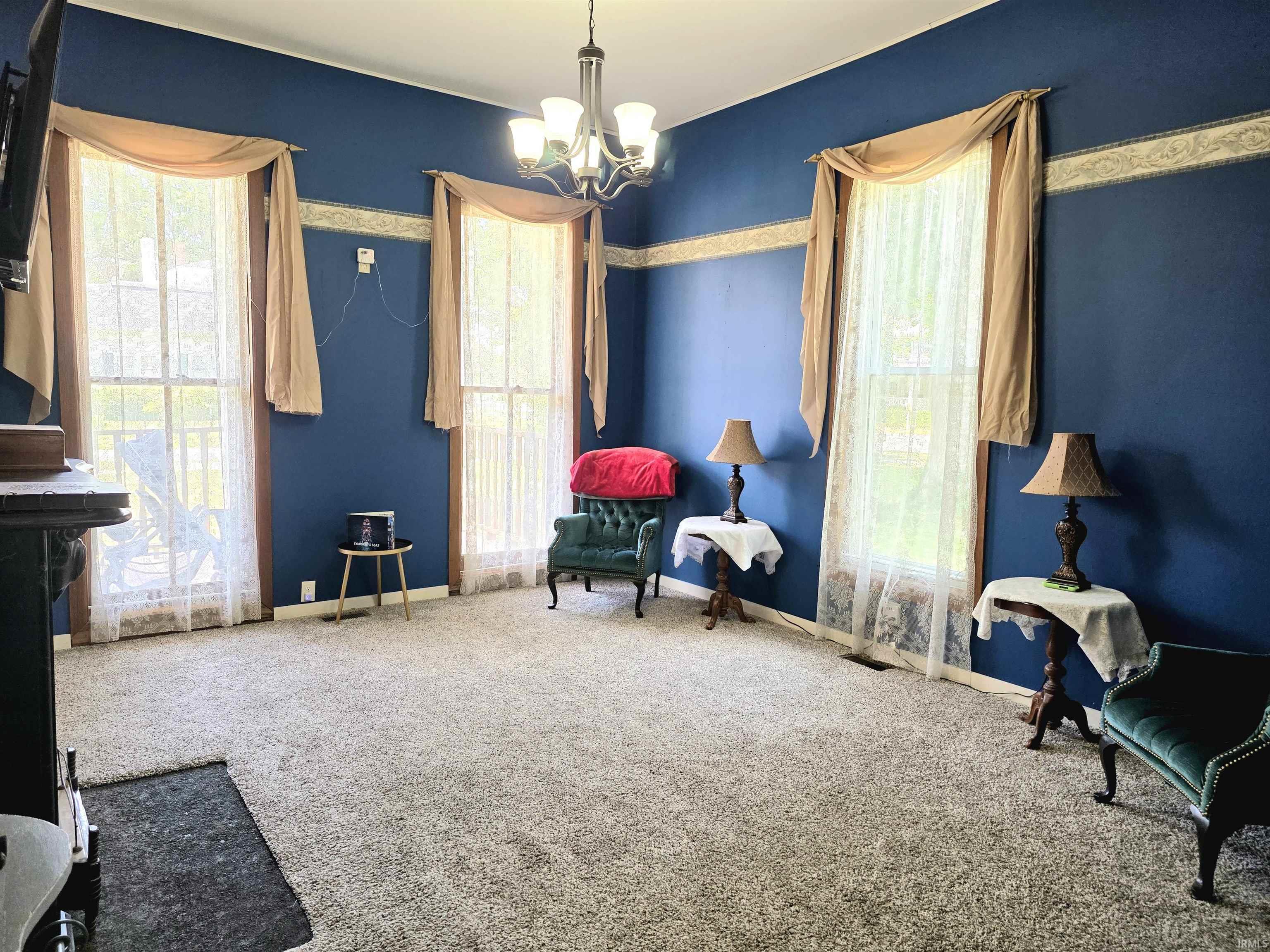 Spacious interior room featuring wall-to-wall carpeting, multiple windows with draped valances, and a ceiling-mounted chandelier