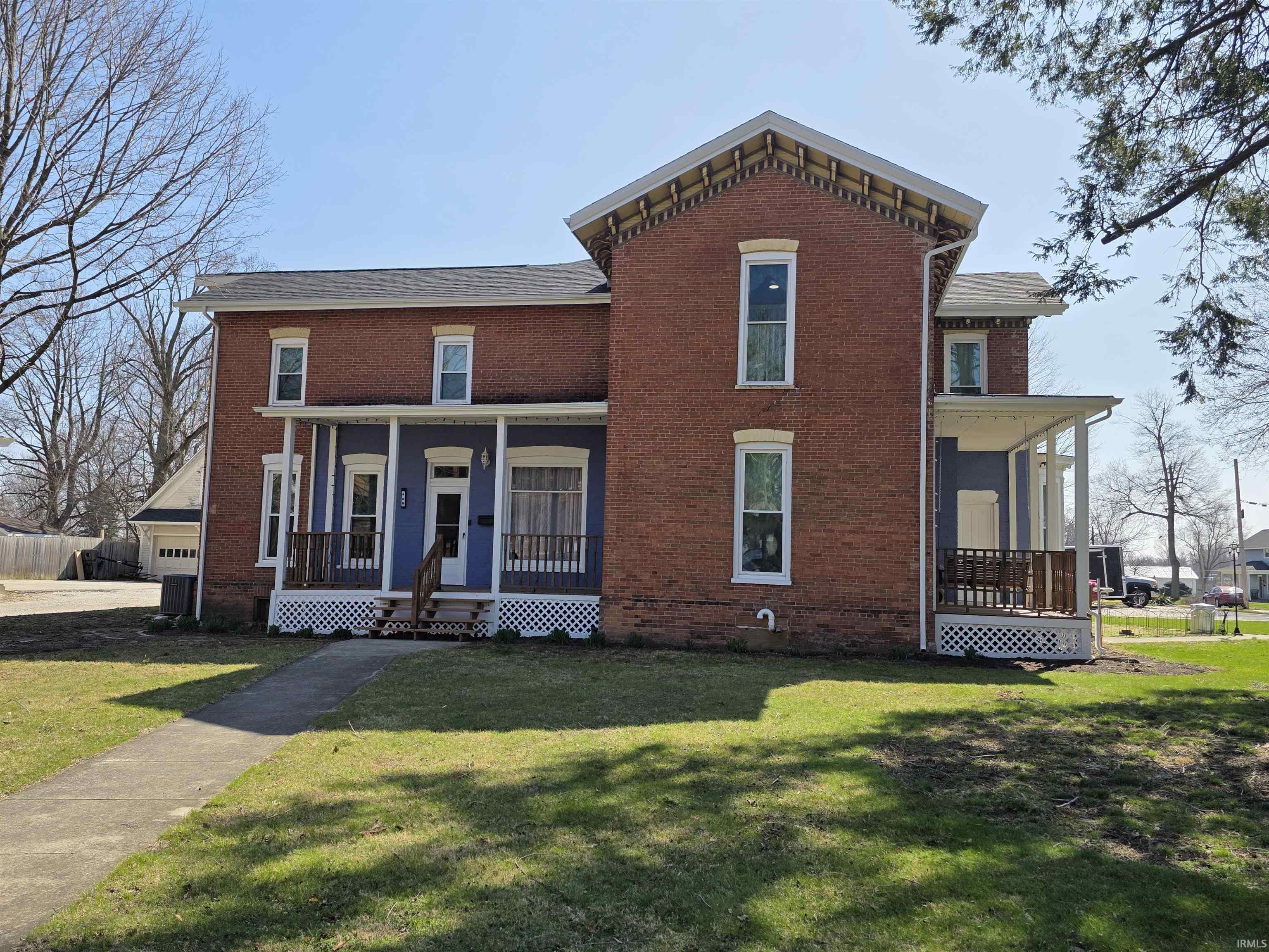 Italianate house featuring covered porch, brick siding, and a front lawn Painting is scheduled when the weather stays warm enough