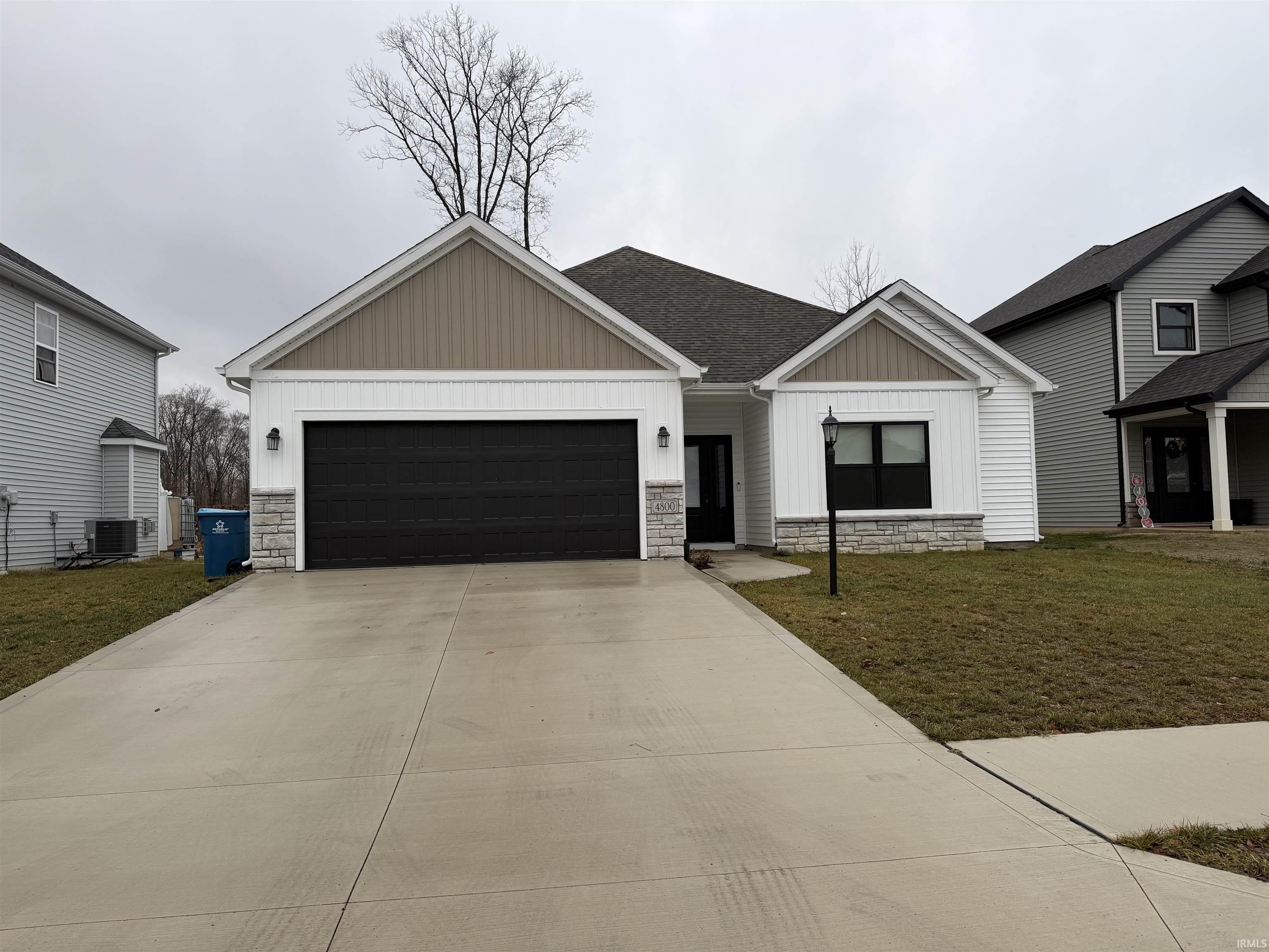 View of front of property featuring board and batten siding, stone siding, and a front lawn