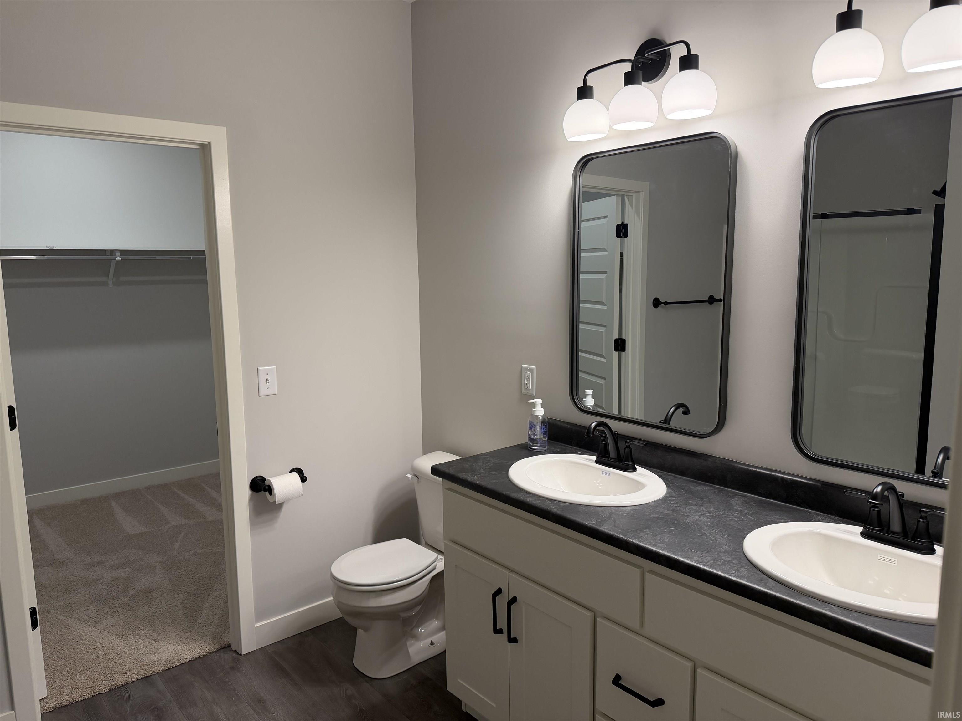 Full bathroom featuring double vanity, a spacious closet, dark wood finished floors, and a shower