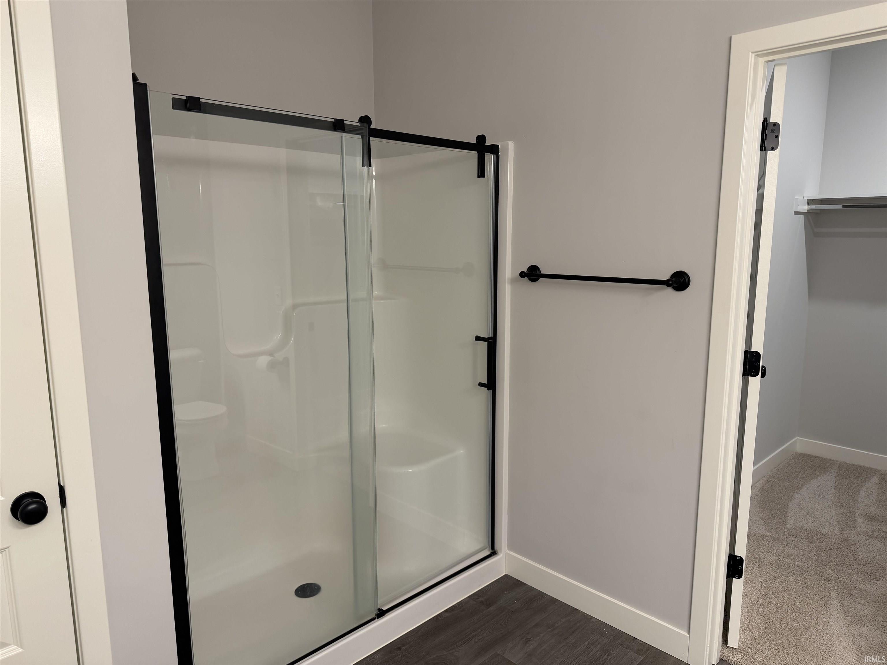 Bathroom with a stall shower, a spacious closet, and dark wood-type flooring