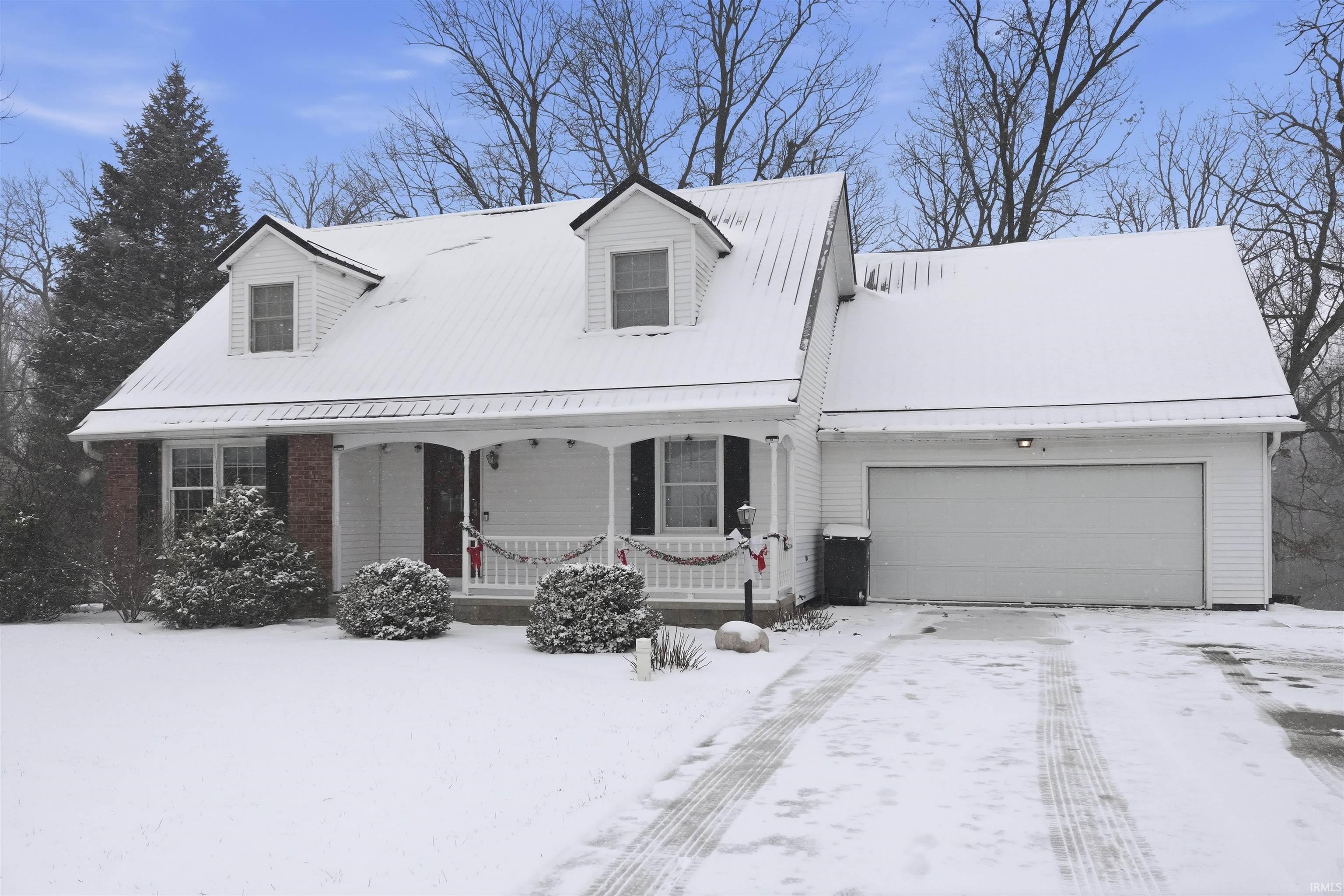 Cape cod house with covered porch, an attached garage, driveway, and brick siding