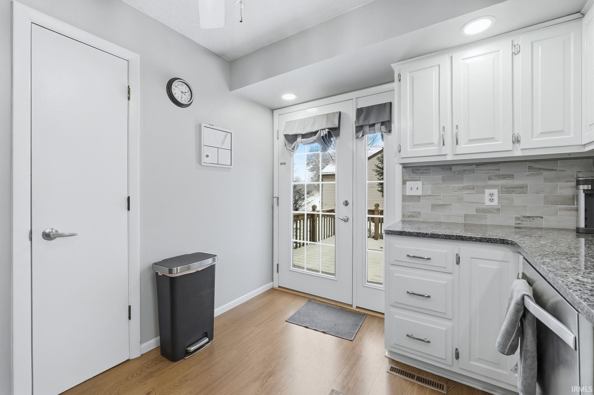 Kitchen featuring white cabinetry, dark stone countertops, backsplash, stainless steel dishwasher, and recessed lighting