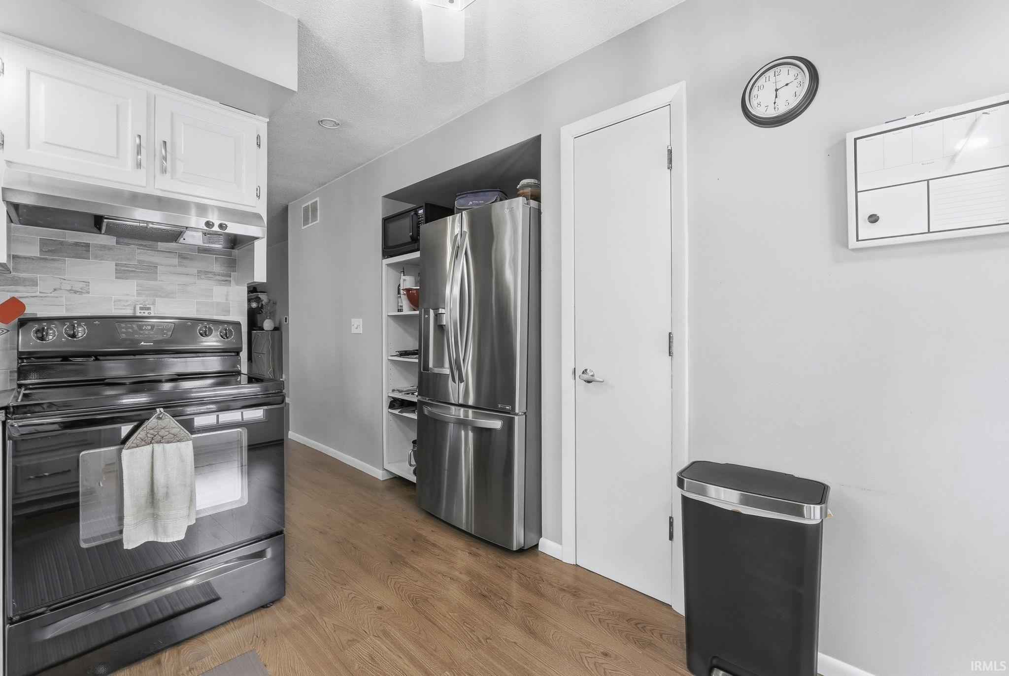 Kitchen with black appliances, white cabinetry, under cabinet range hood, tasteful backsplash, and dark wood finished floors