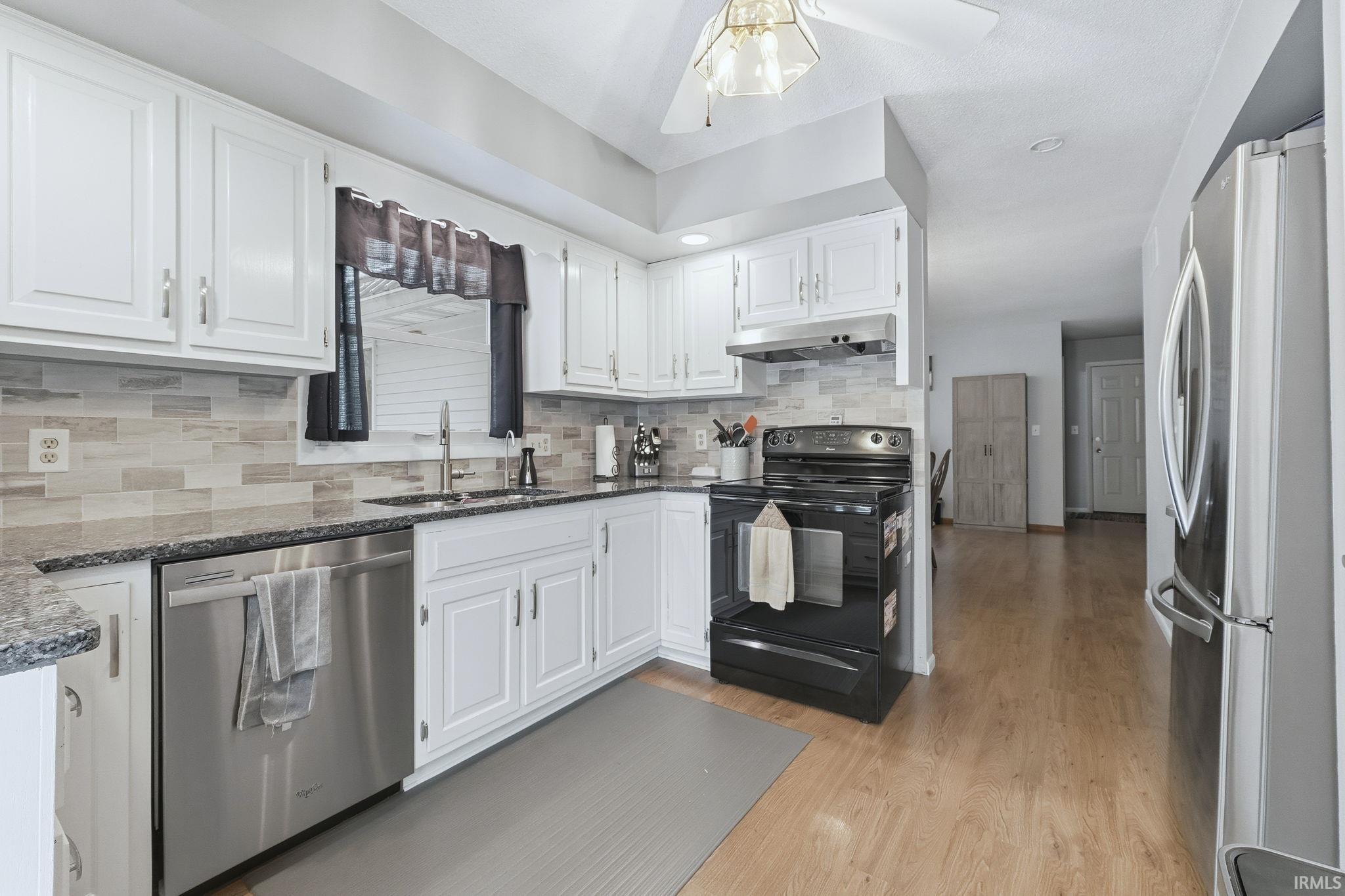Kitchen with stainless steel appliances, white cabinetry, dark stone counters, light wood-type flooring, and tasteful backsplash