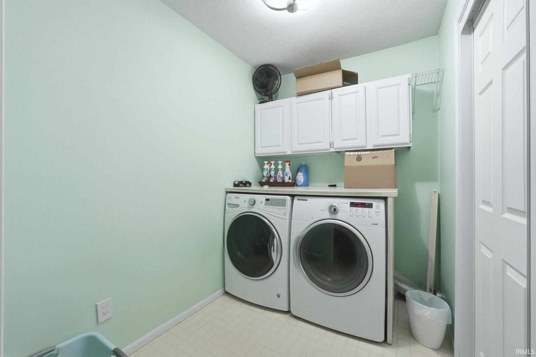Laundry area with light flooring, cabinet space, washer and clothes dryer, and a textured ceiling