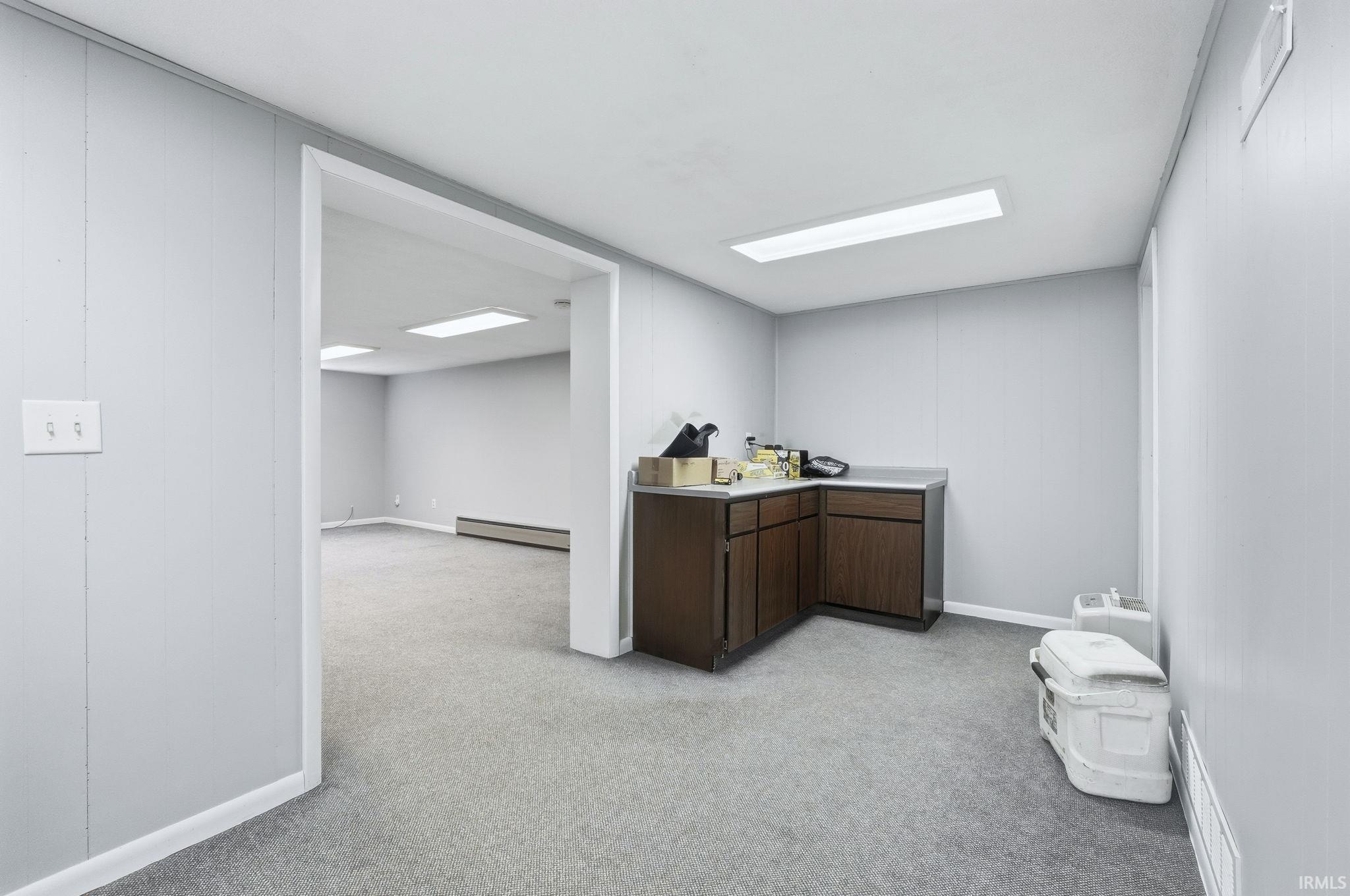 Bar with dark brown cabinetry, light countertops, light colored carpet, and baseboard heating