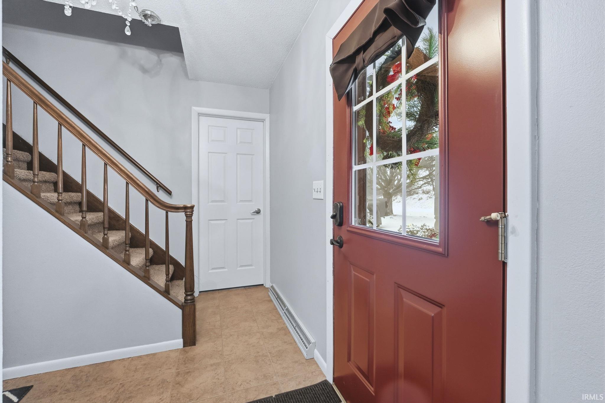 Entryway with a baseboard heating unit, stairs, and light tile patterned flooring