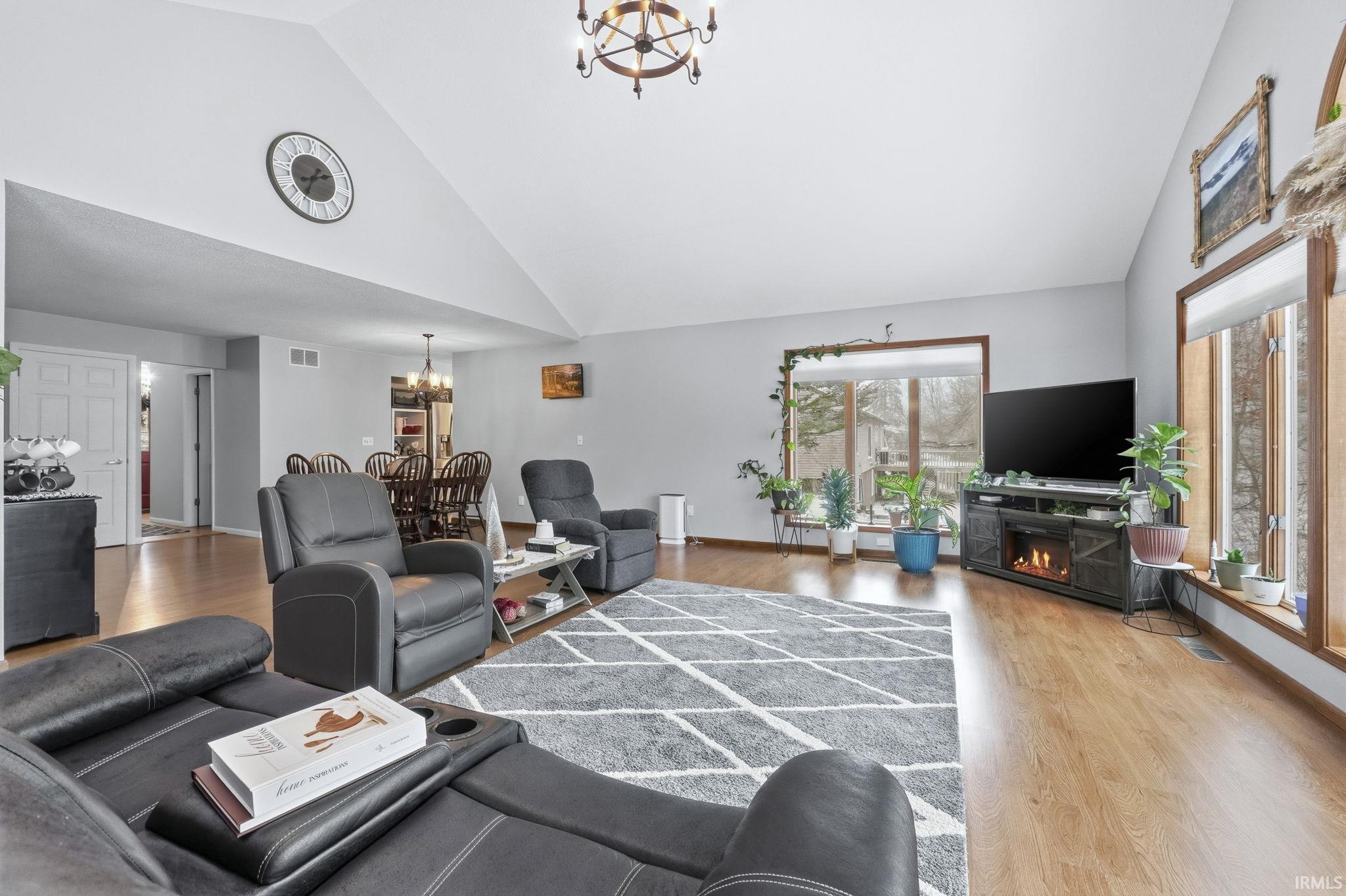 Living room with a chandelier, wood finished floors, high vaulted ceiling, and a lit fireplace