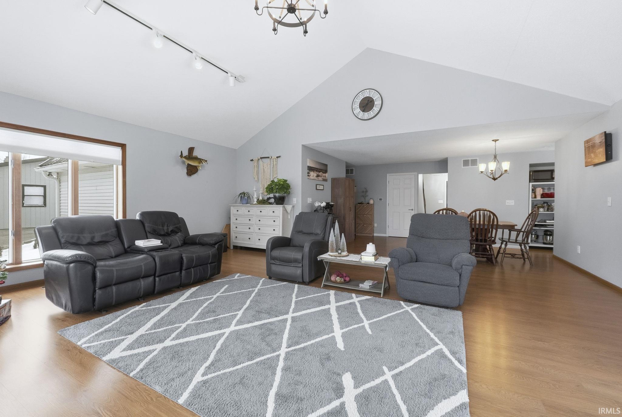 Living area featuring a chandelier, light wood-type flooring, rail lighting, and high vaulted ceiling