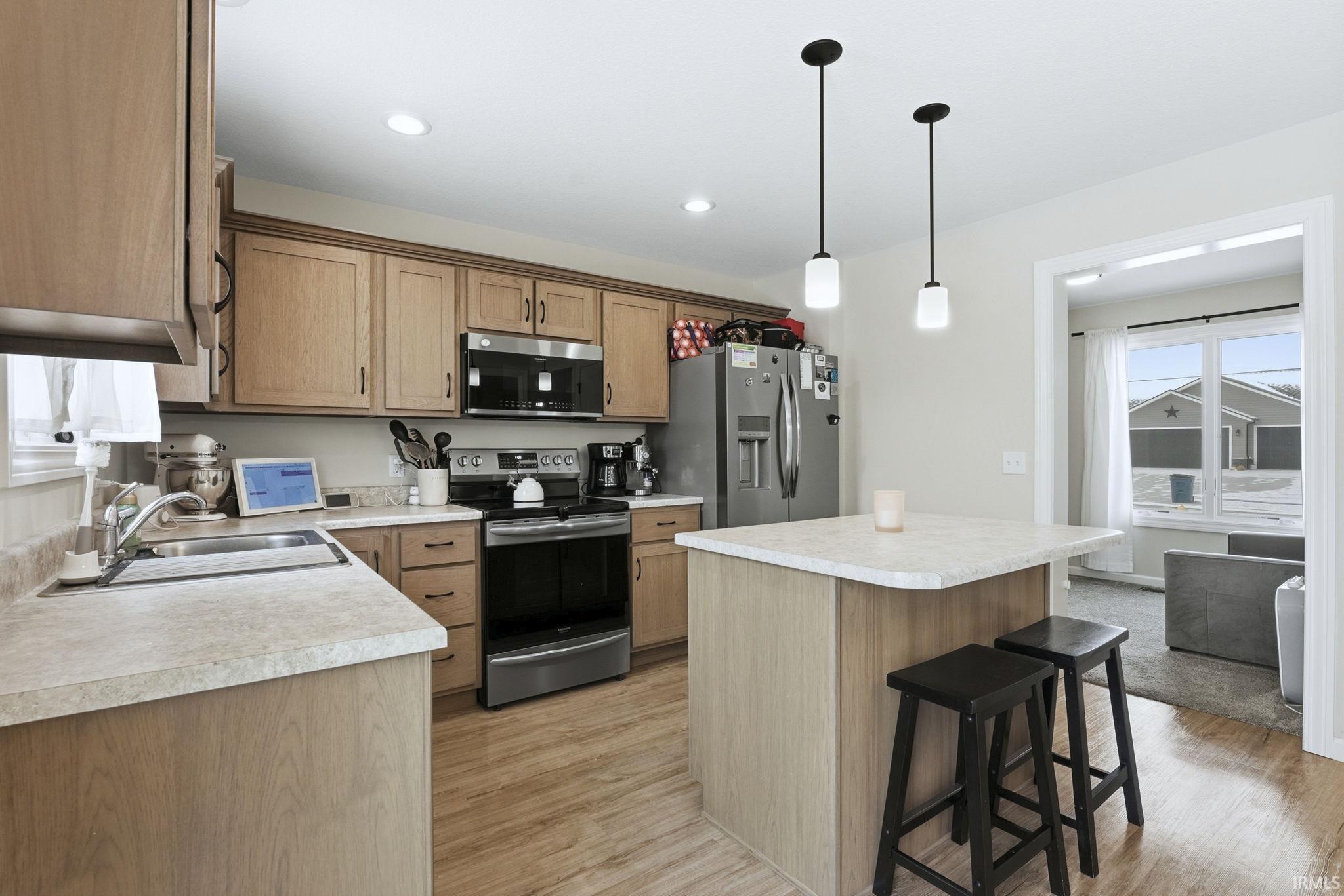 Kitchen featuring a kitchen bar, appliances with stainless steel finishes, a center island, hanging light fixtures, and light wood-type flooring