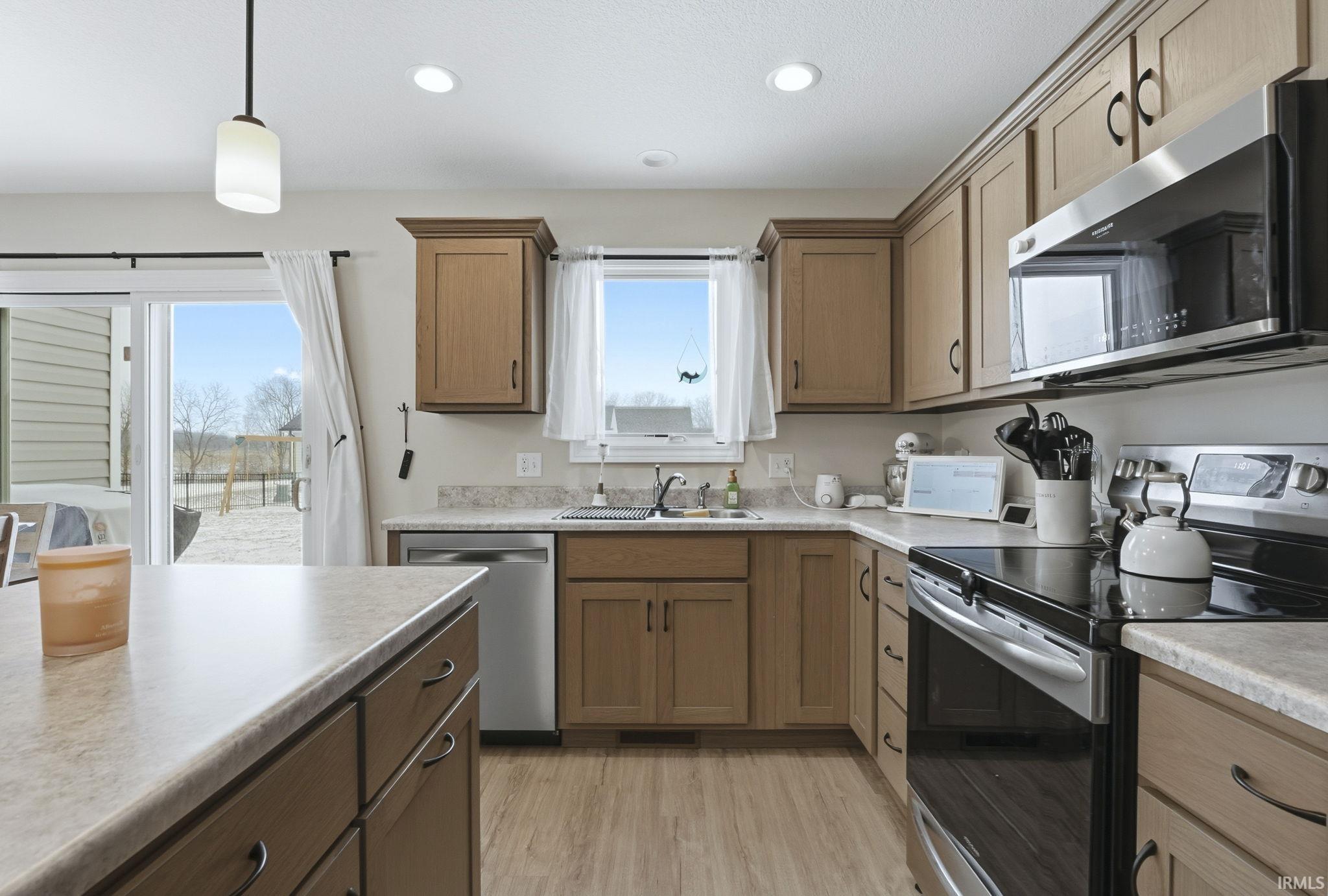 Kitchen with appliances with stainless steel finishes, decorative light fixtures, brown cabinetry, light countertops, and recessed lighting