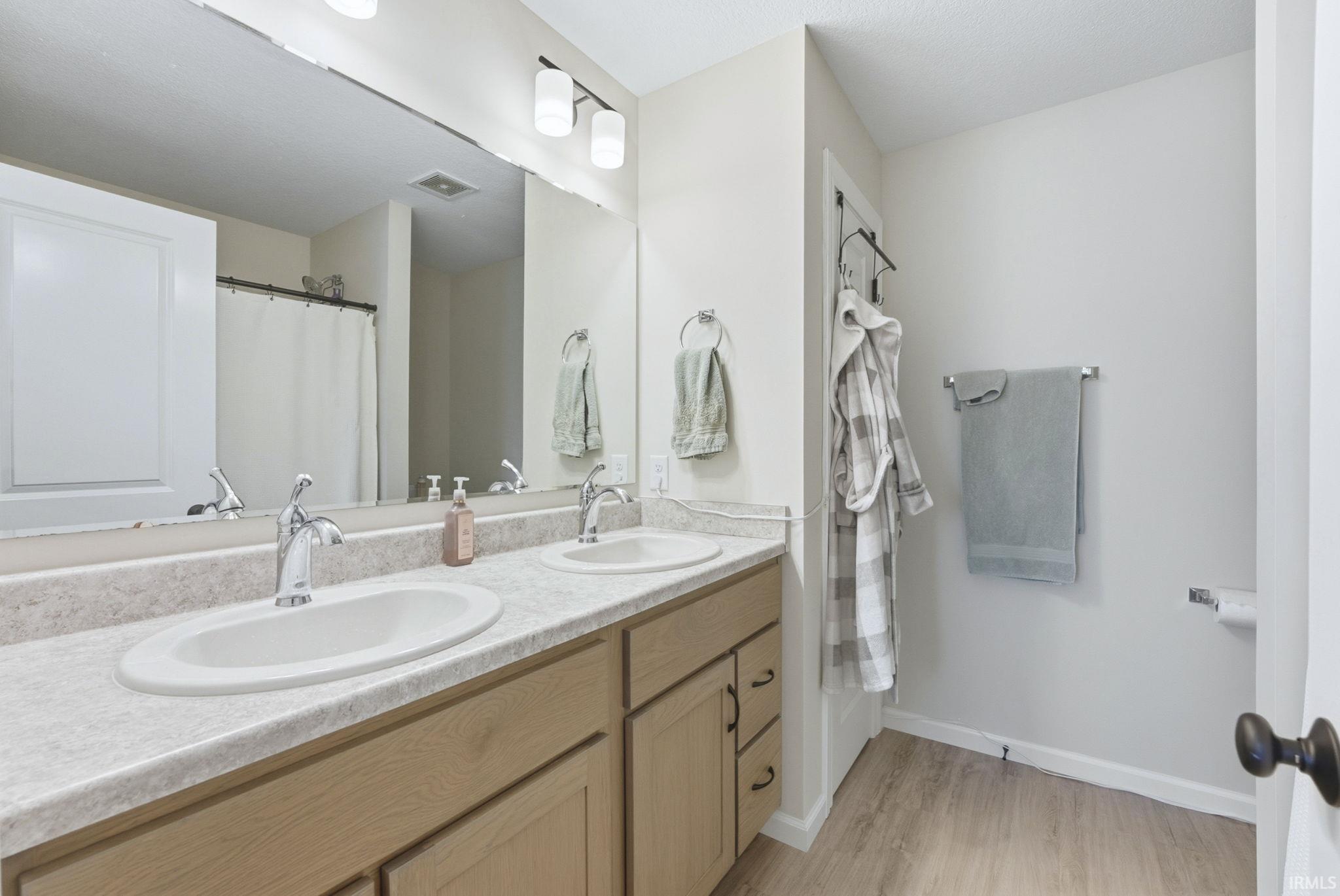 Bathroom featuring a shower with curtain, double vanity, and light wood-style flooring