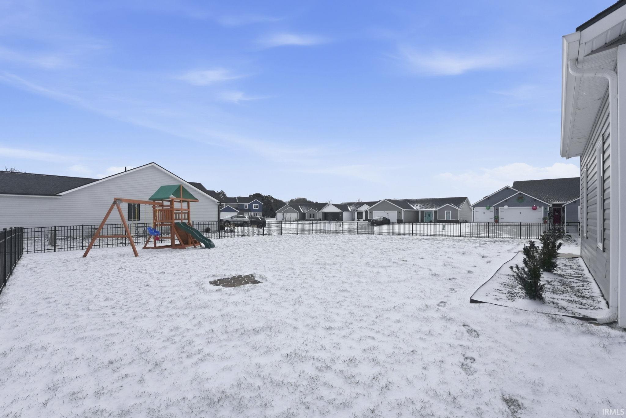 Yard layered in snow featuring a fenced backyard, a residential view, and a playground