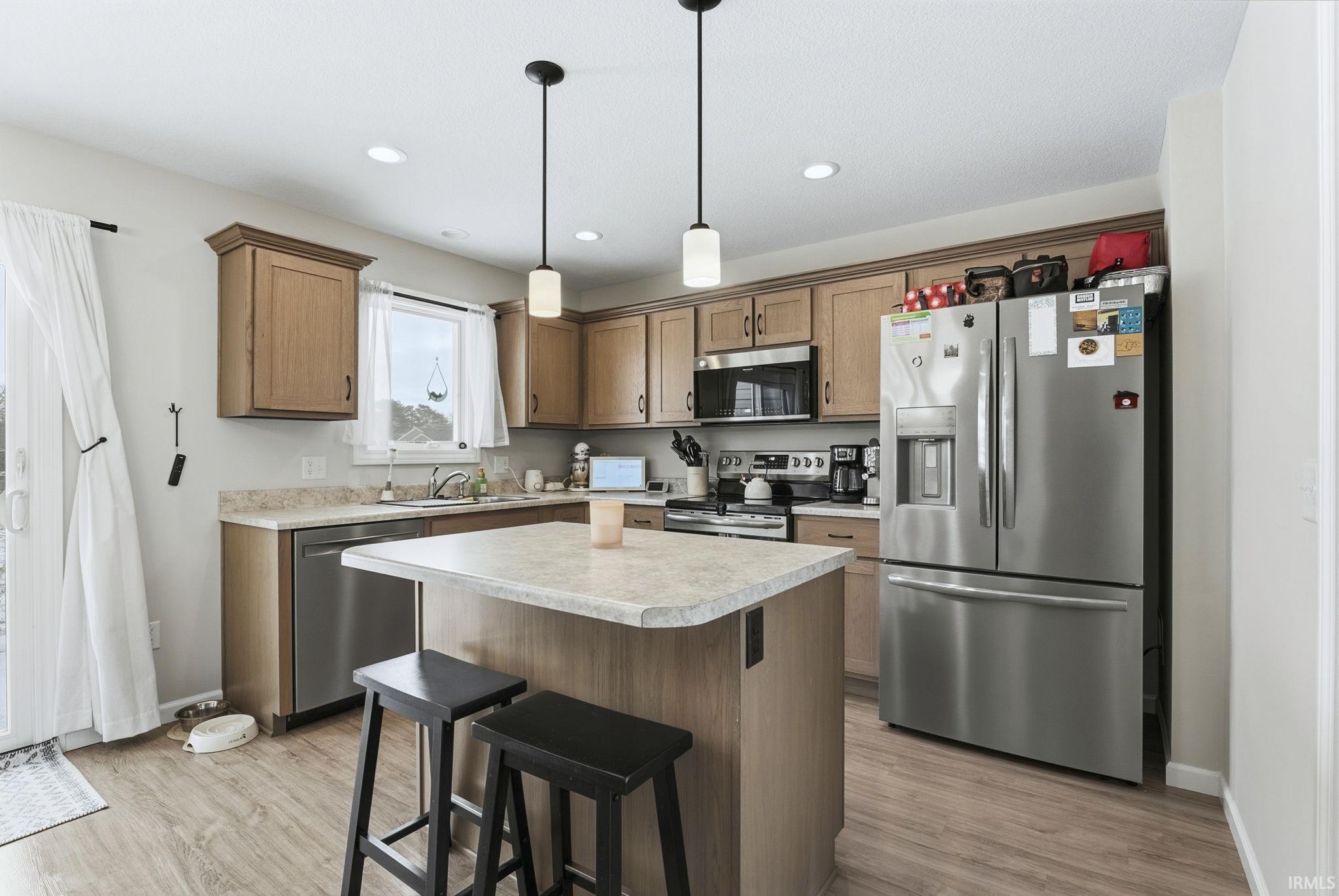 Kitchen with a center island, stainless steel appliances, a kitchen breakfast bar, light countertops, and decorative light fixtures
