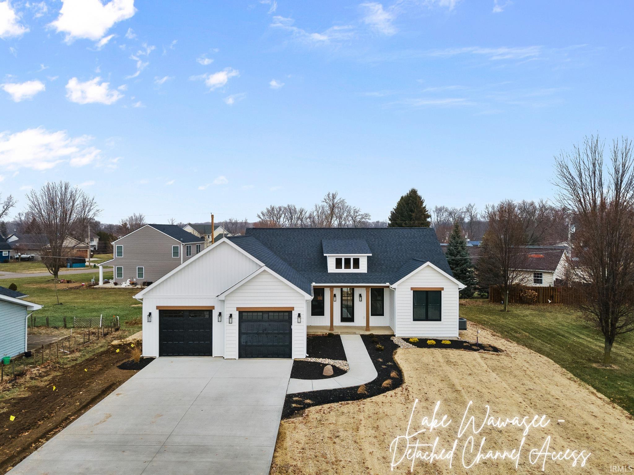 Modern inspired farmhouse featuring large concrete driveway, natural wood accents, seeded yard, attached garage w/black doors and neutral trim details