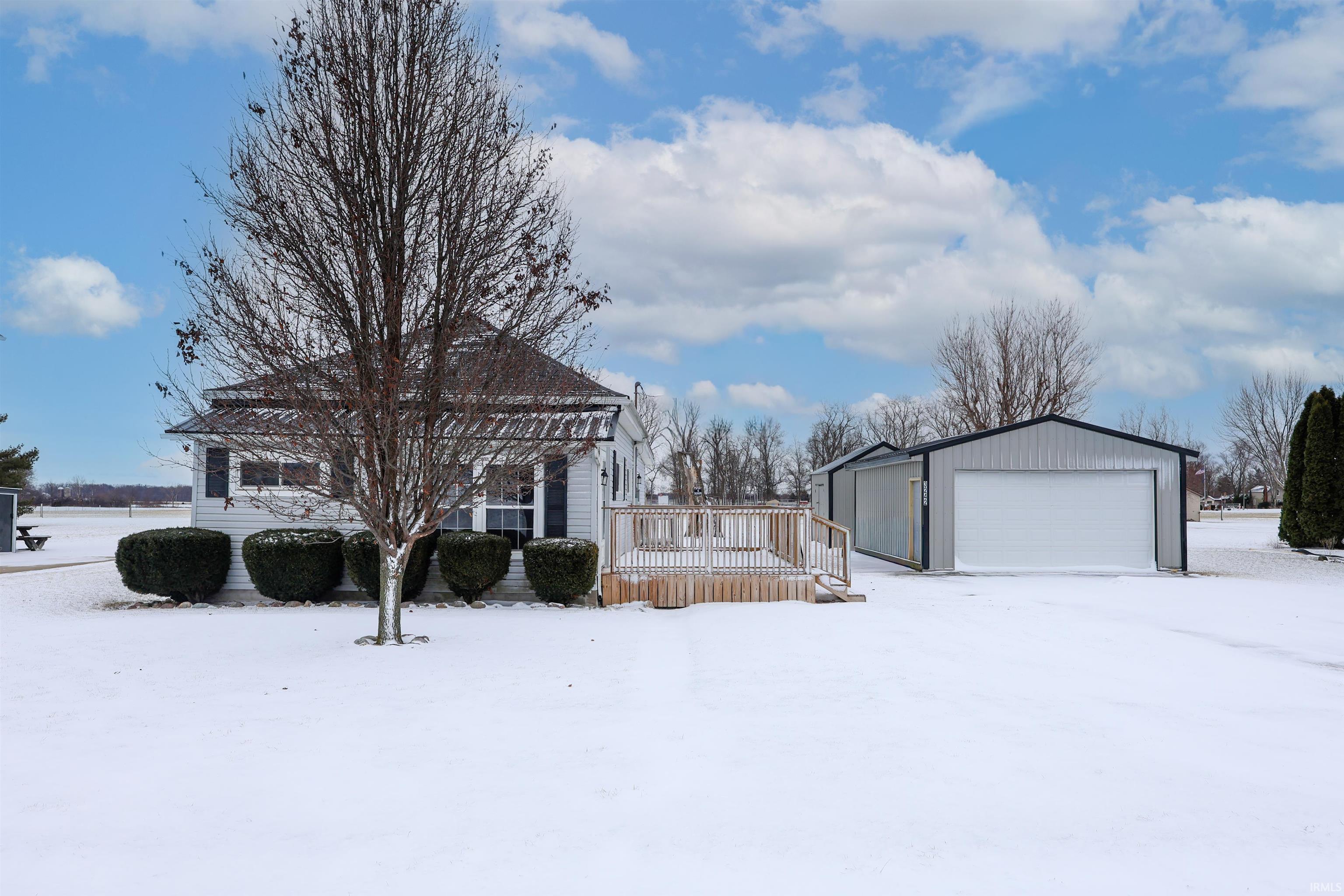 View of snowy exterior featuring a deck, an outdoor structure, and a detached garage