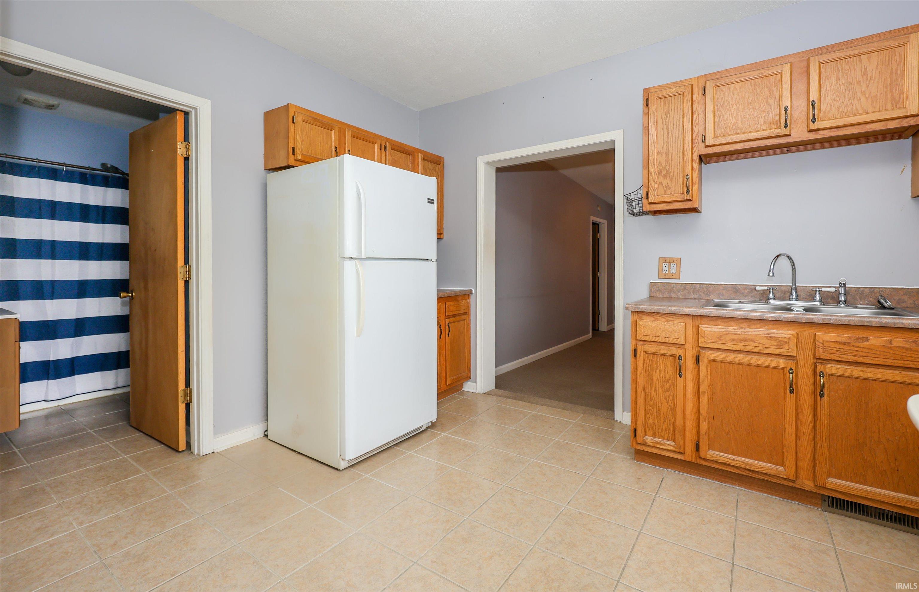 Kitchen with freestanding refrigerator, light countertops, brown cabinets, and light tile patterned flooring