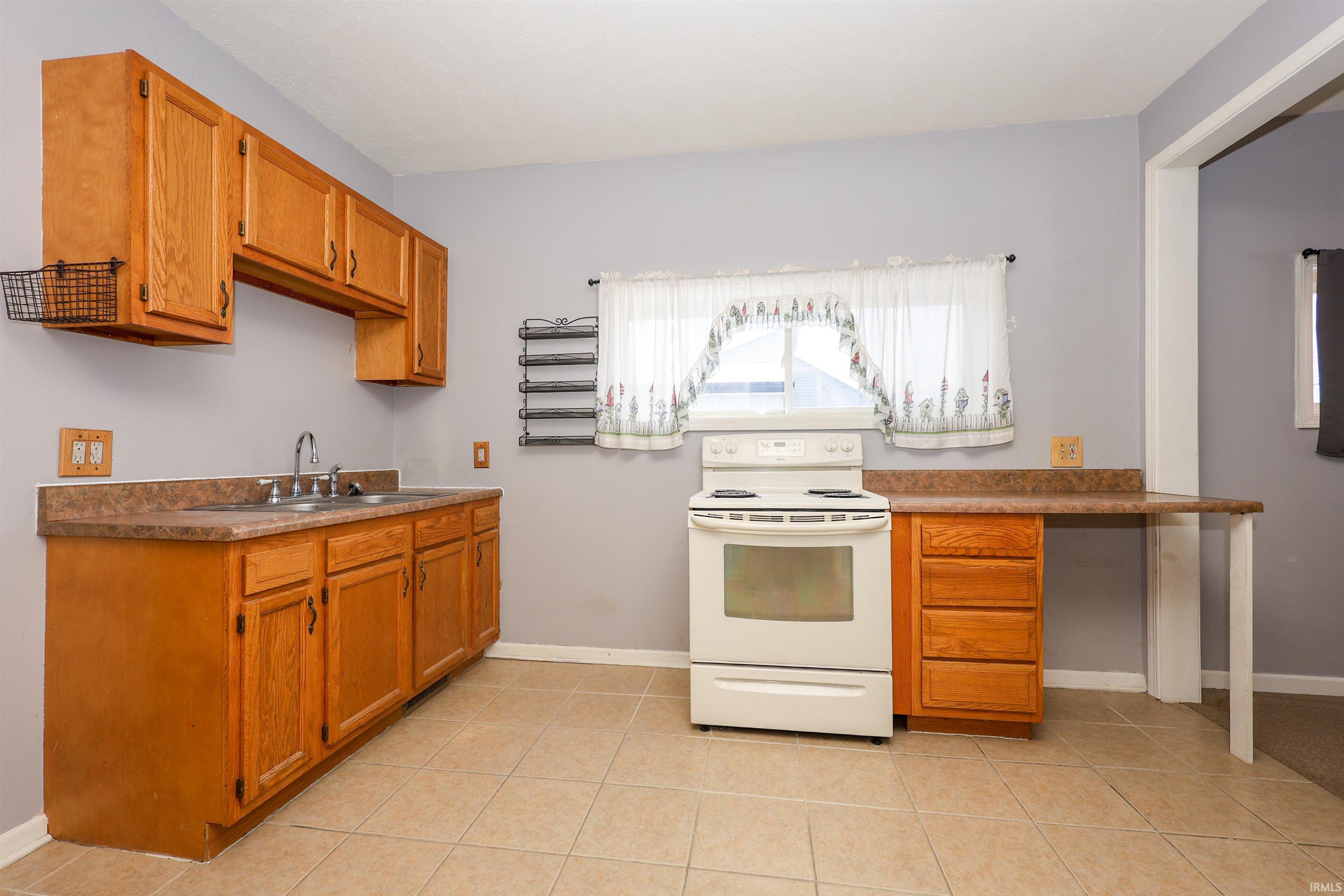 Kitchen with electric range, brown cabinetry, and light tile patterned floors