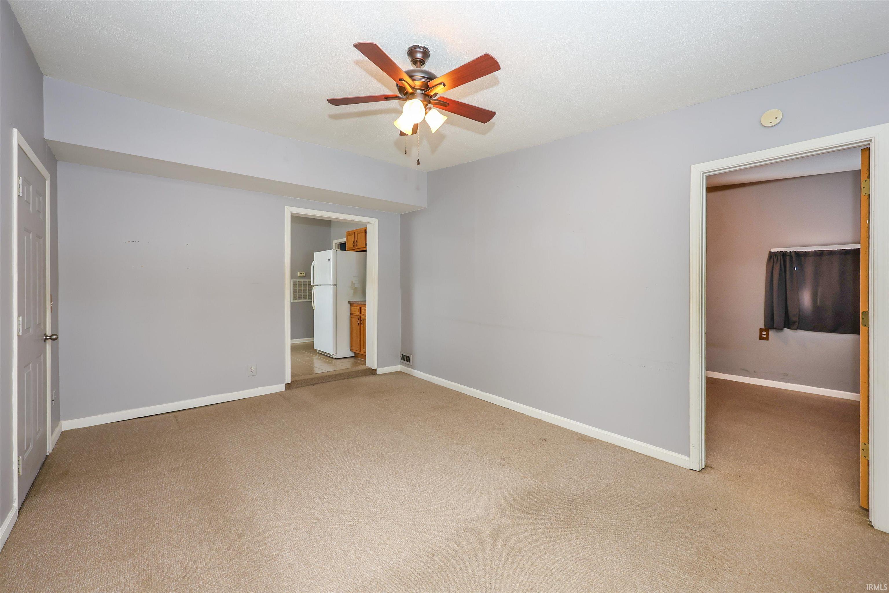 Unfurnished bedroom with freestanding refrigerator, light colored carpet, and a ceiling fan