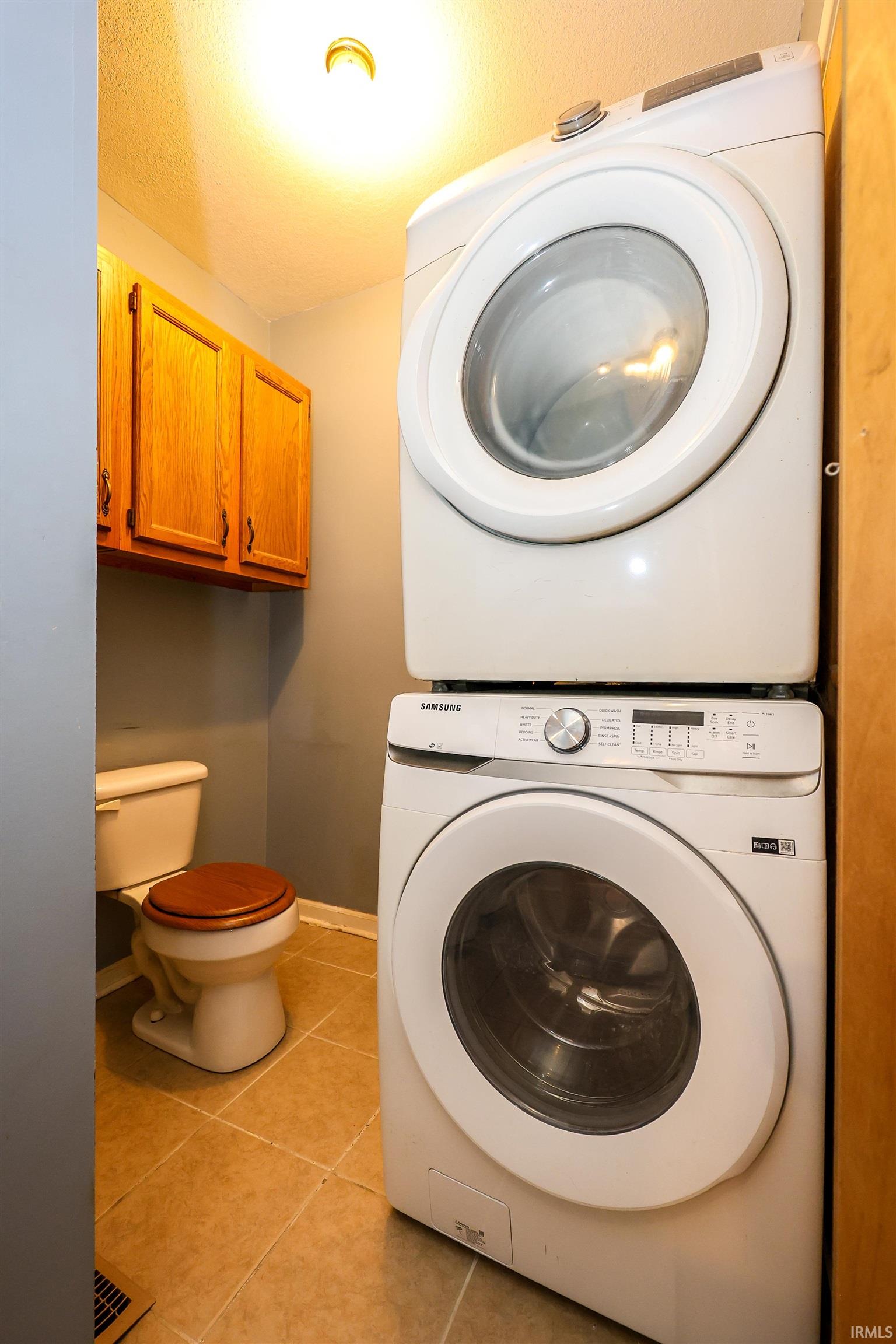 Laundry area featuring stacked washer / drying machine, light tile patterned floors, and a textured ceiling