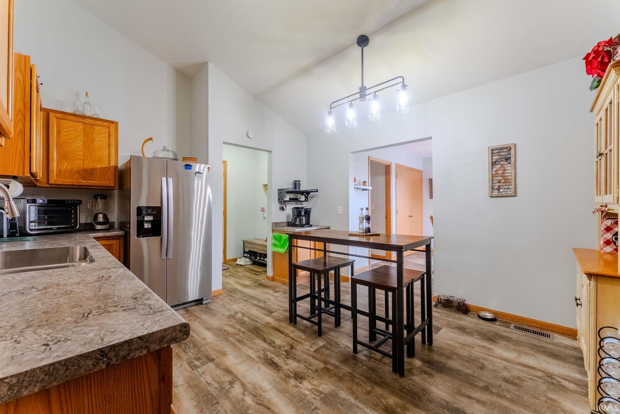 Kitchen with stainless steel fridge with ice dispenser, brown cabinets, high vaulted ceiling, light wood-style flooring, and decorative light fixtures
