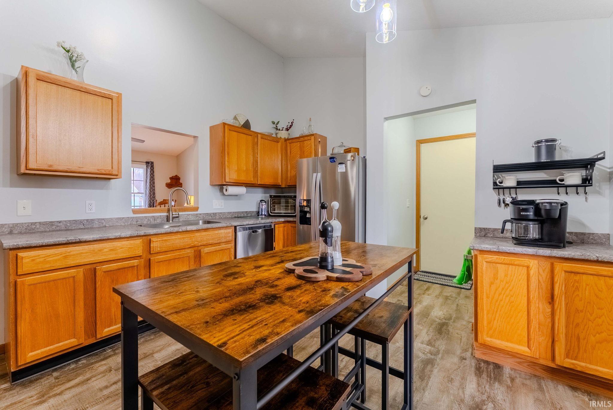 Kitchen with stainless steel appliances, light countertops, light wood-style floors, brown cabinetry, and high vaulted ceiling
