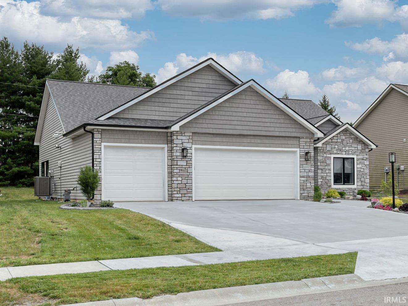 View of front of home with stone siding, driveway, a garage, and a front lawn