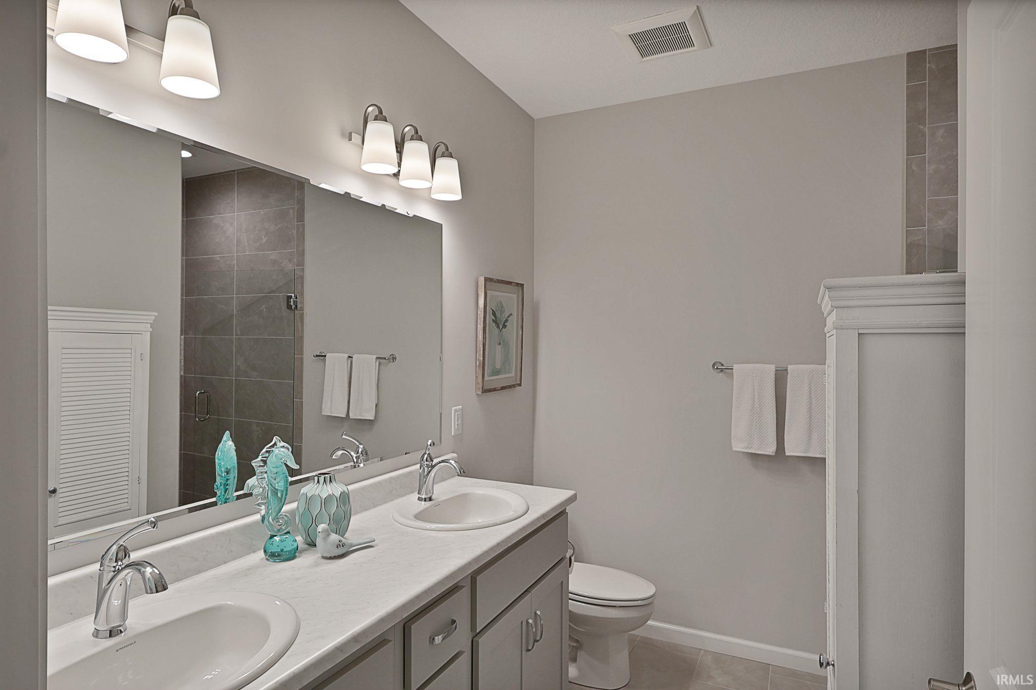 Full bath featuring double vanity, a tile shower, and light tile patterned flooring