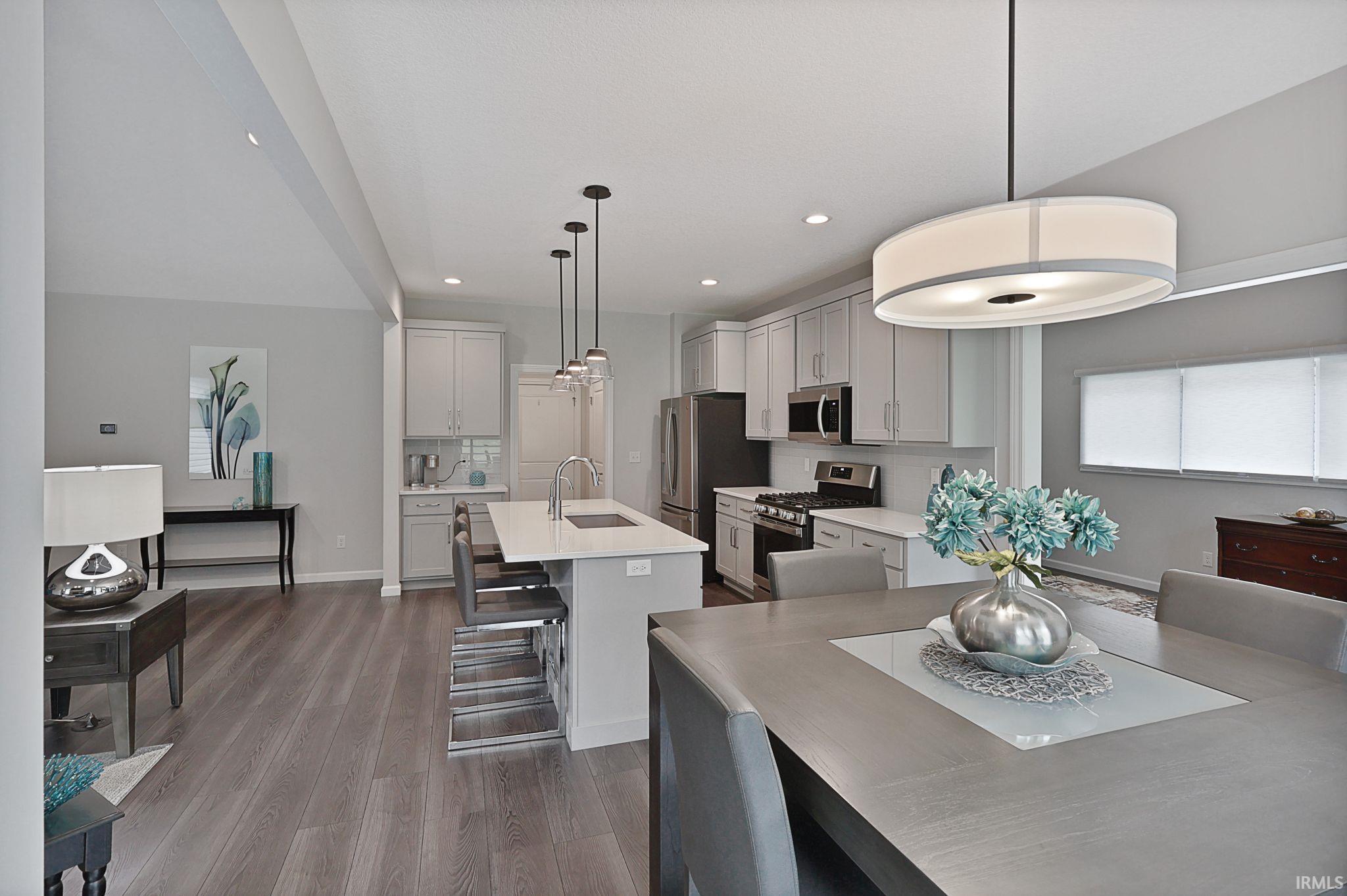 Kitchen featuring stainless steel appliances, hanging light fixtures, a kitchen bar, a kitchen island with sink, and dark wood-style flooring