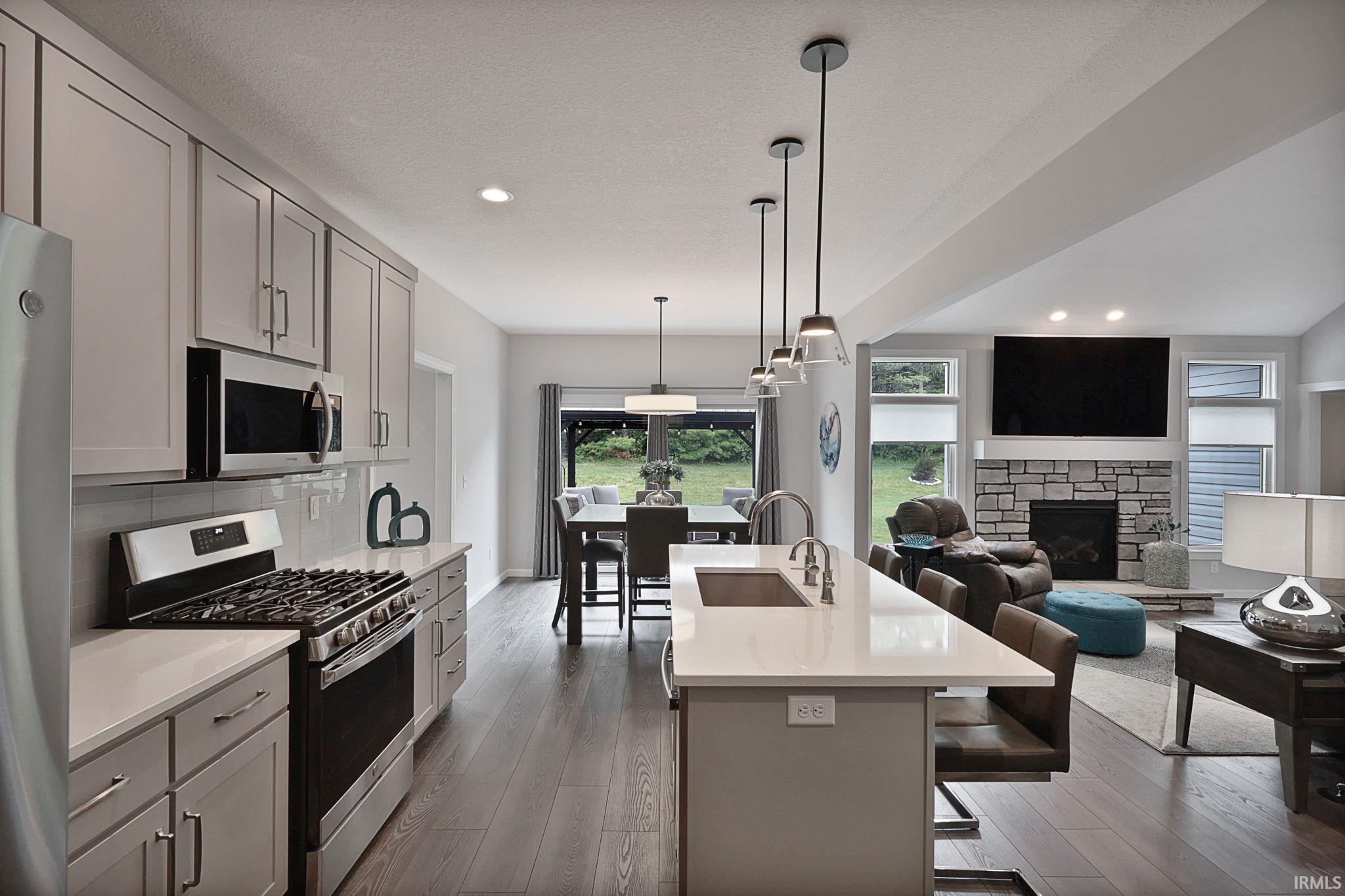 Kitchen featuring gray cabinetry, stainless steel appliances, hanging light fixtures, a fireplace, and a kitchen breakfast bar