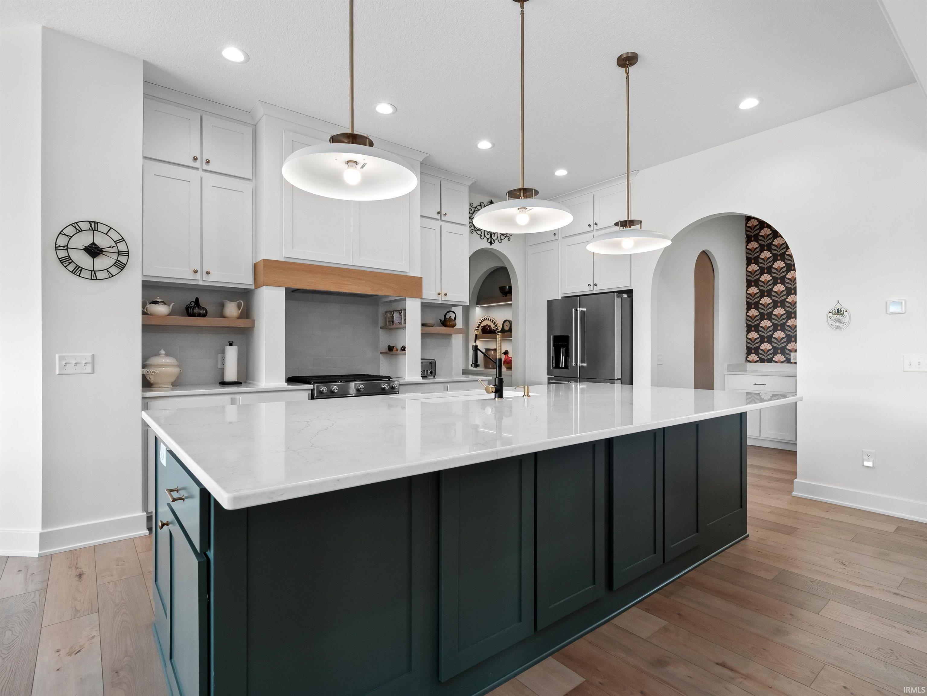 Kitchen featuring white cabinetry, open shelves, high end refrigerator, arched walkways, and a large island with sink
