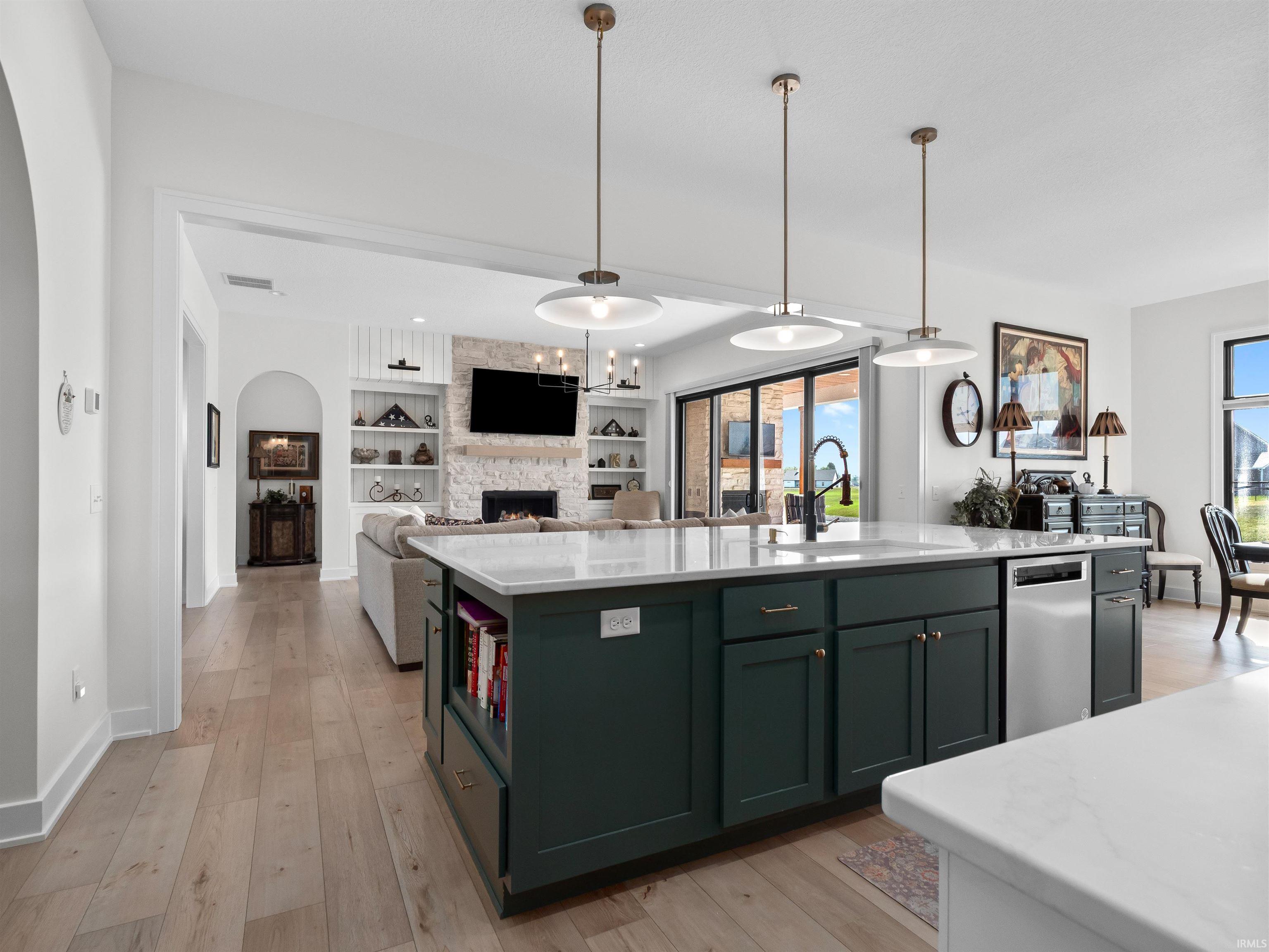 Kitchen featuring light stone counters, pendant lighting, open floor plan, built in features, and an island with sink