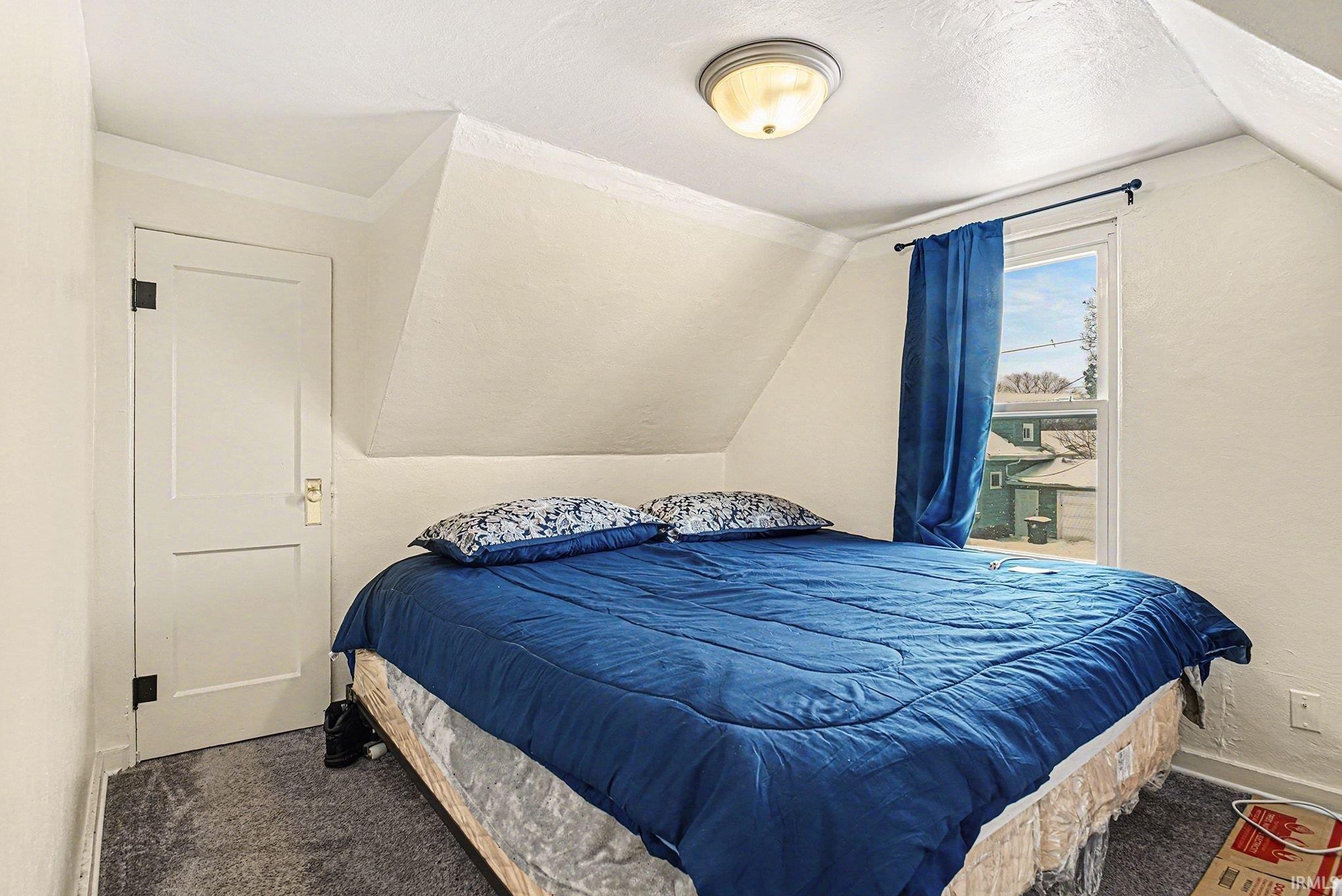 Carpeted bedroom featuring vaulted ceiling and a textured ceiling